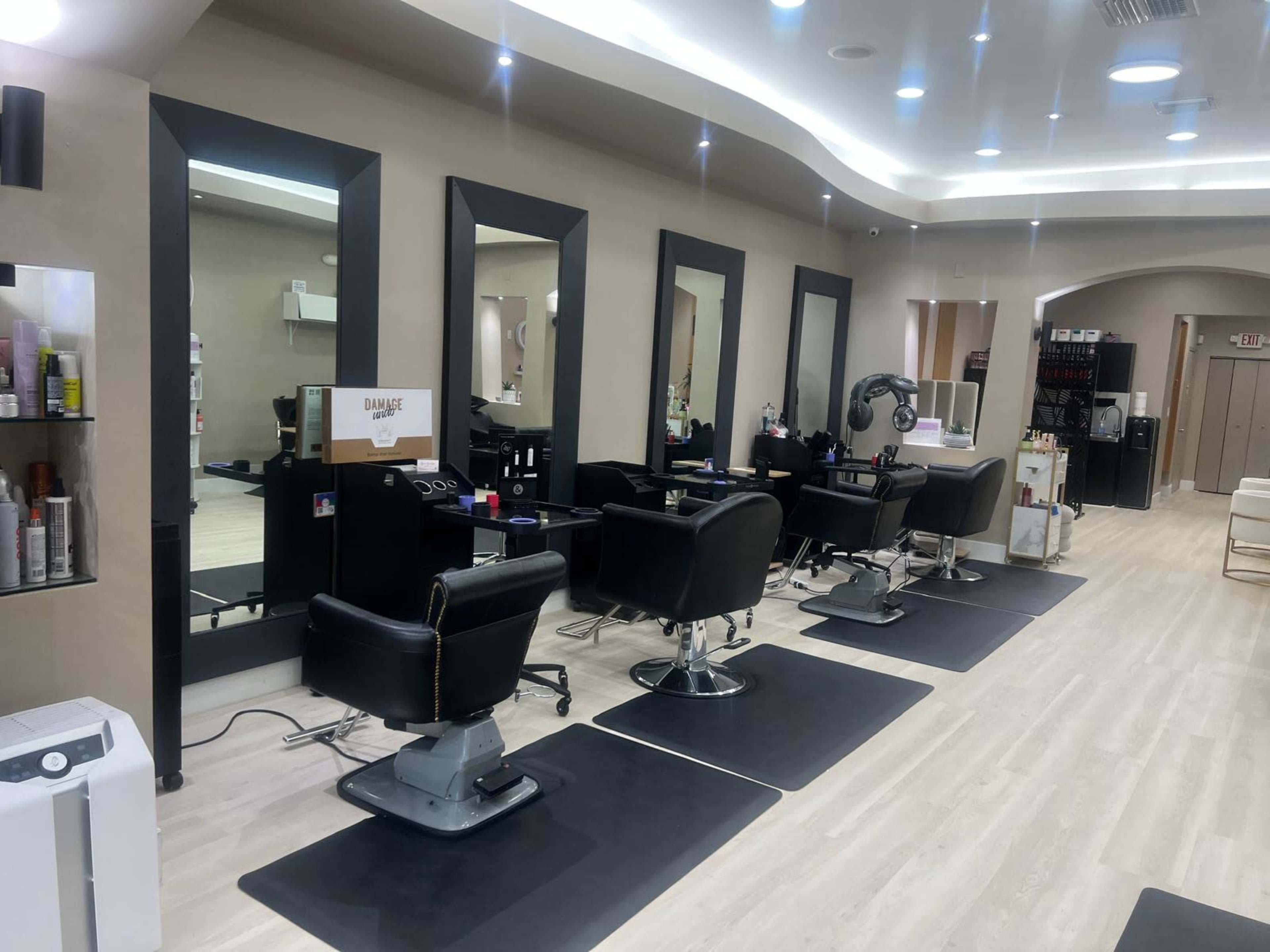 The image shows the interior of a hair salon featuring several black salon chairs, large mirrors, and a sleek, modern design.