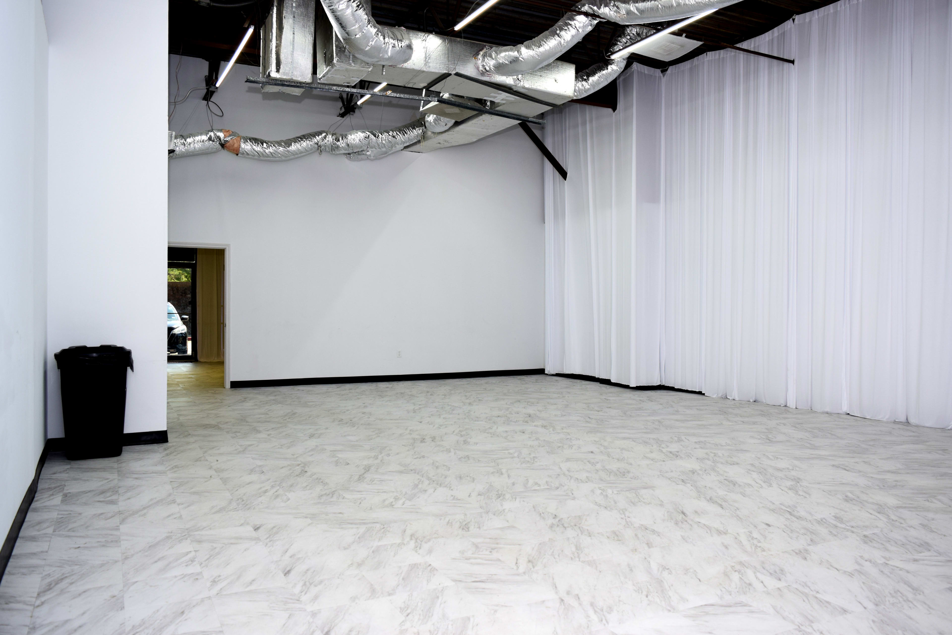 The image shows a spacious, empty room with a marble-patterned floor, white walls, and visible ductwork on the ceiling.