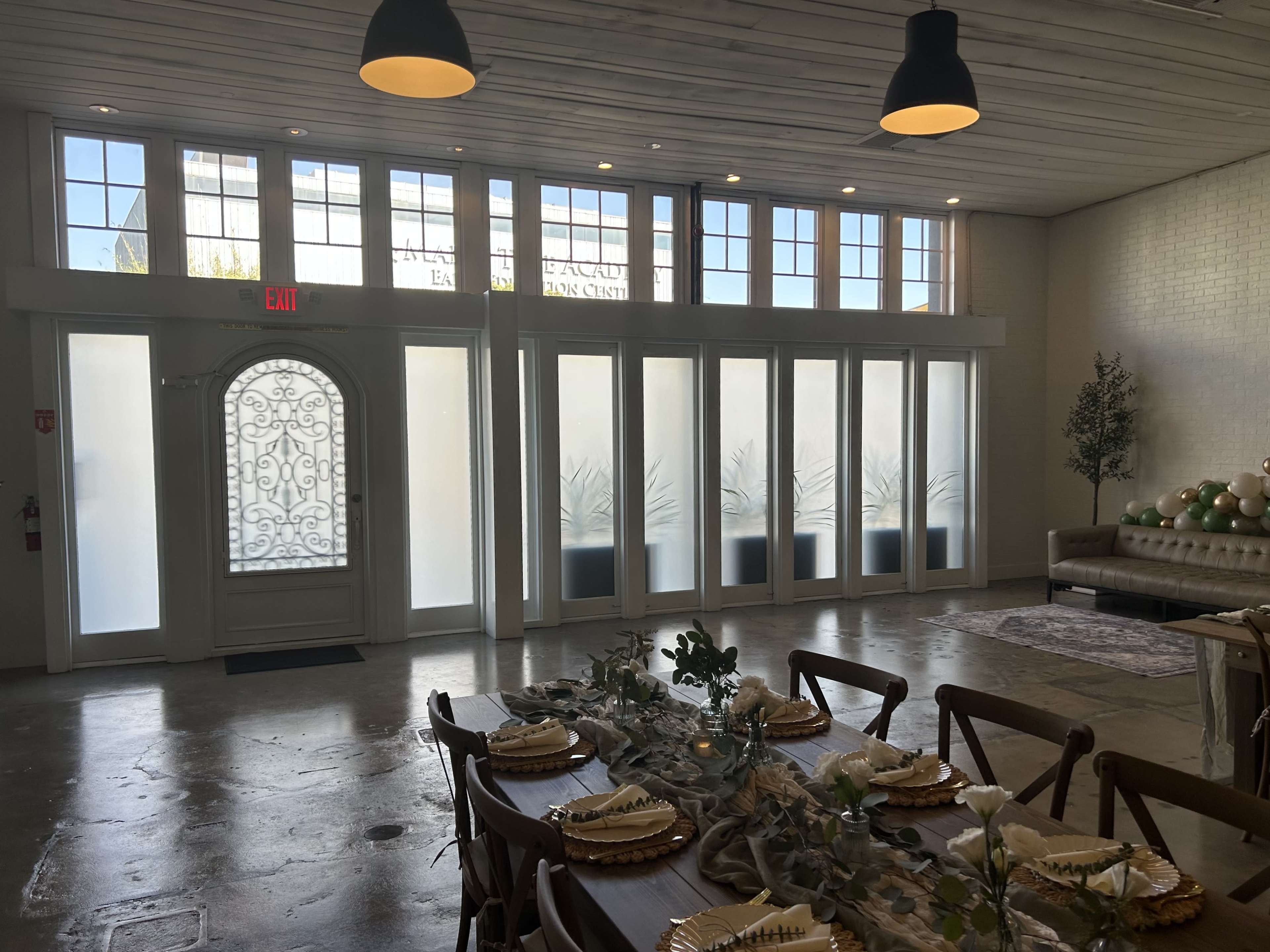 The interior of a venue features a large entrance door, light streaming in through frosted glass panels, and a dining table set with plates and decor.