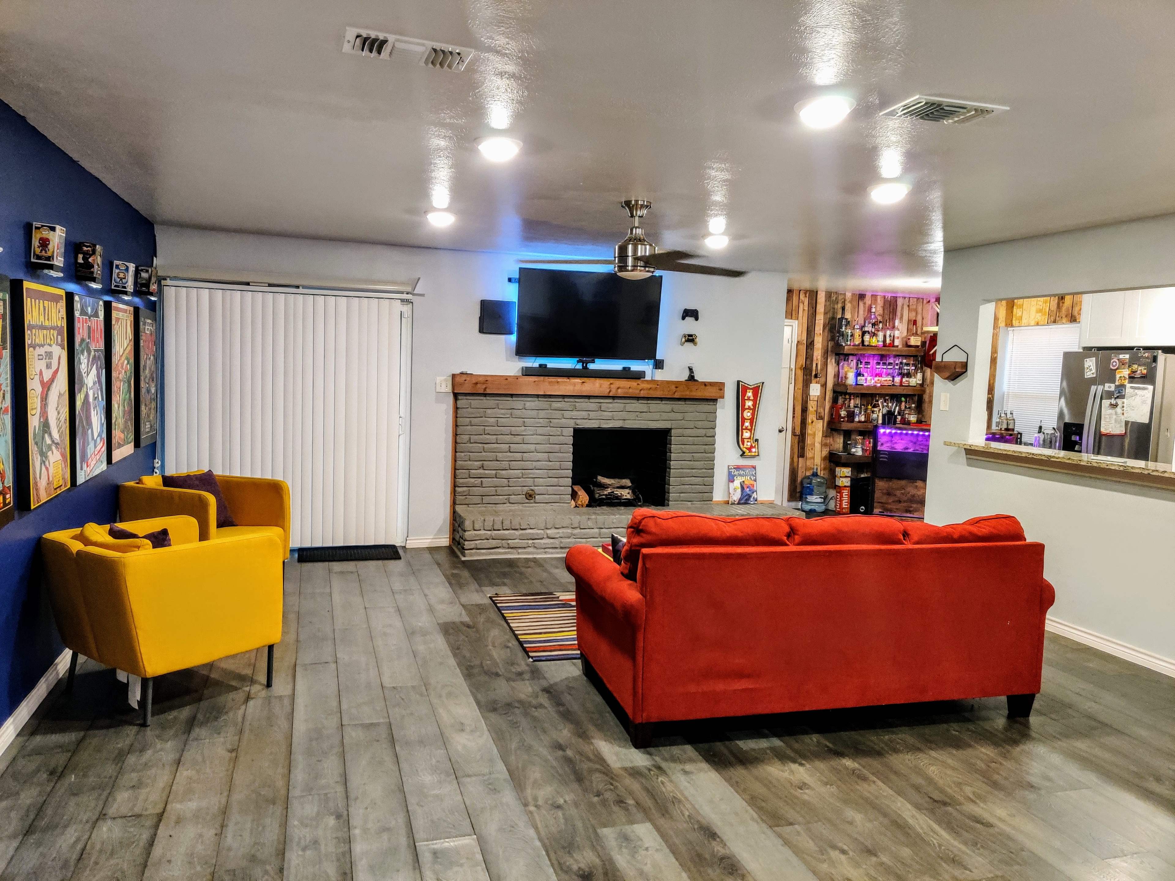 The room features a red sofa and two yellow chairs, a fireplace with a television above it, and a bar area visible through an opening in the wall.