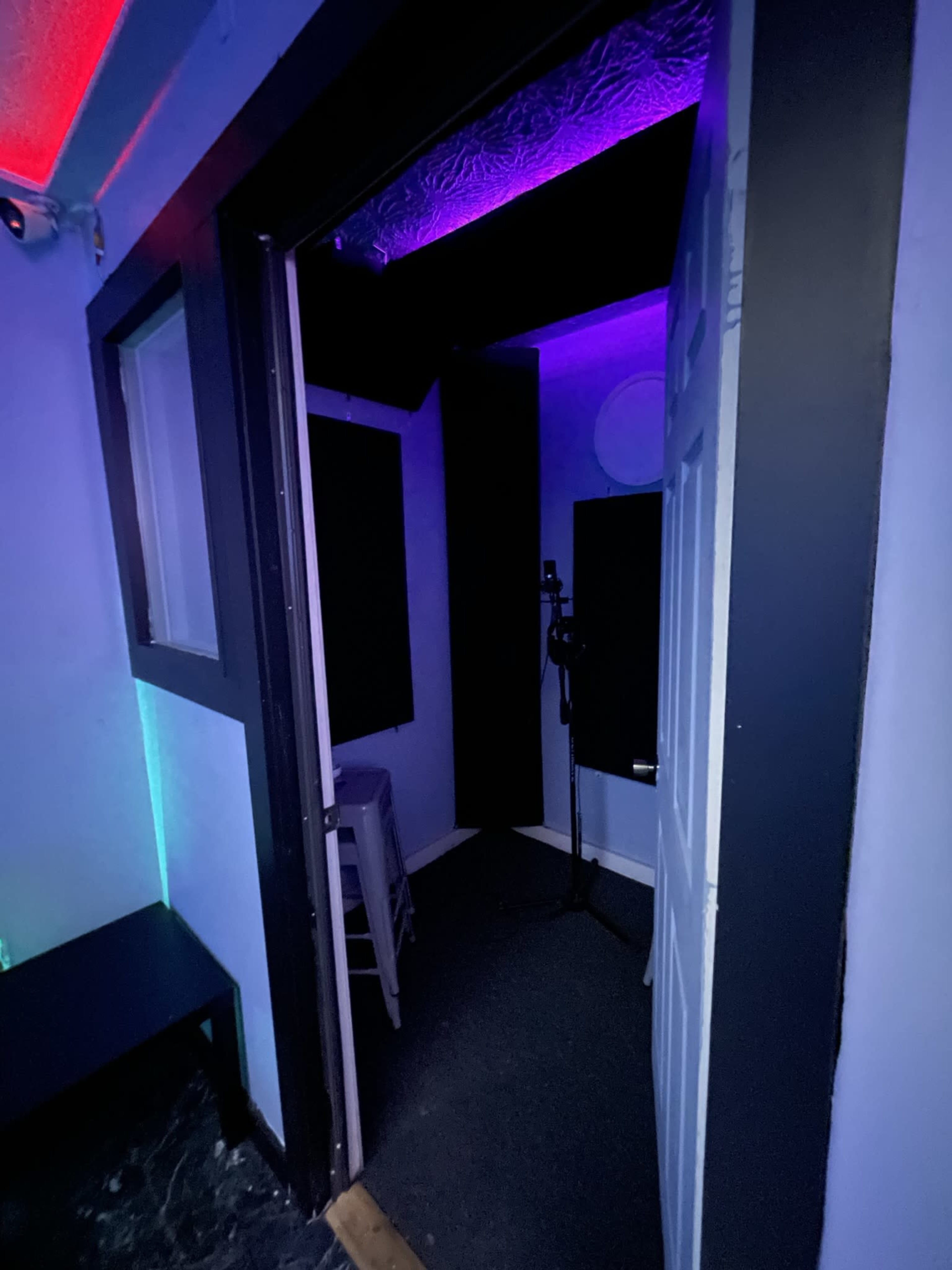 A doorway leading into a small recording booth with walls illuminated by colored lights.