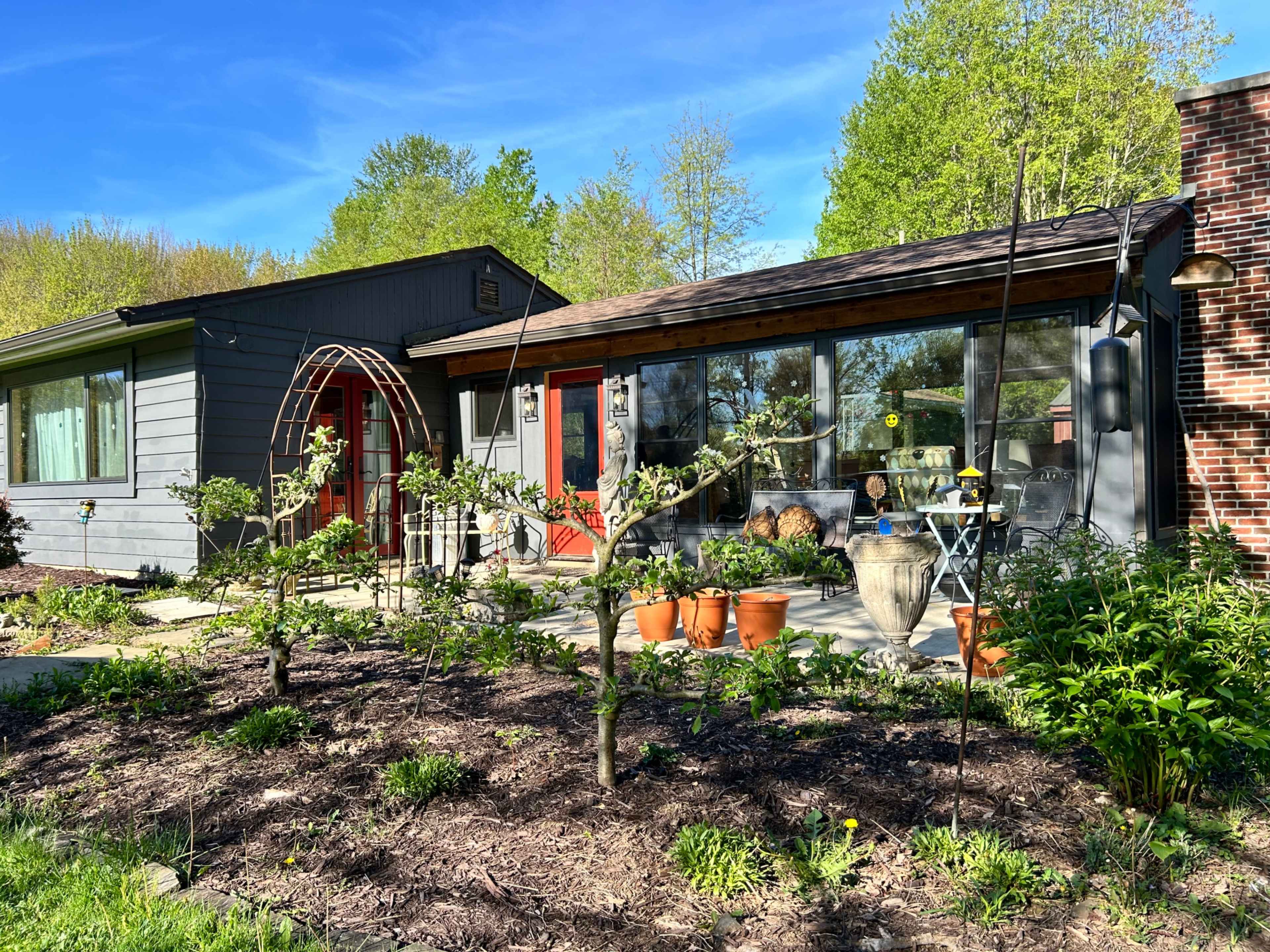 A modern-style house with a landscaped garden featuring small trees and potted plants in the foreground.