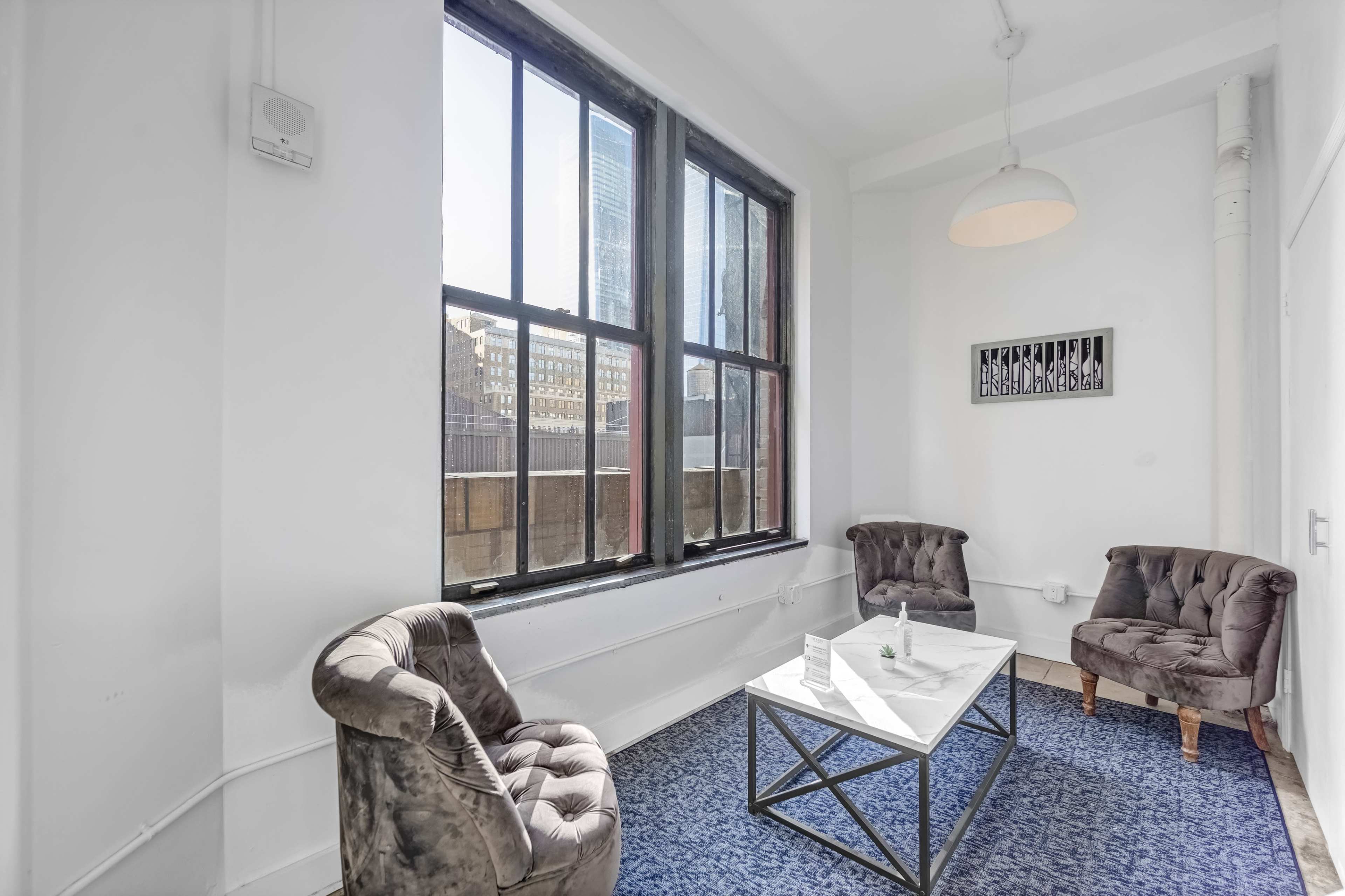 A small room features two tufted chairs, a coffee table, and a large window that lets in natural light.