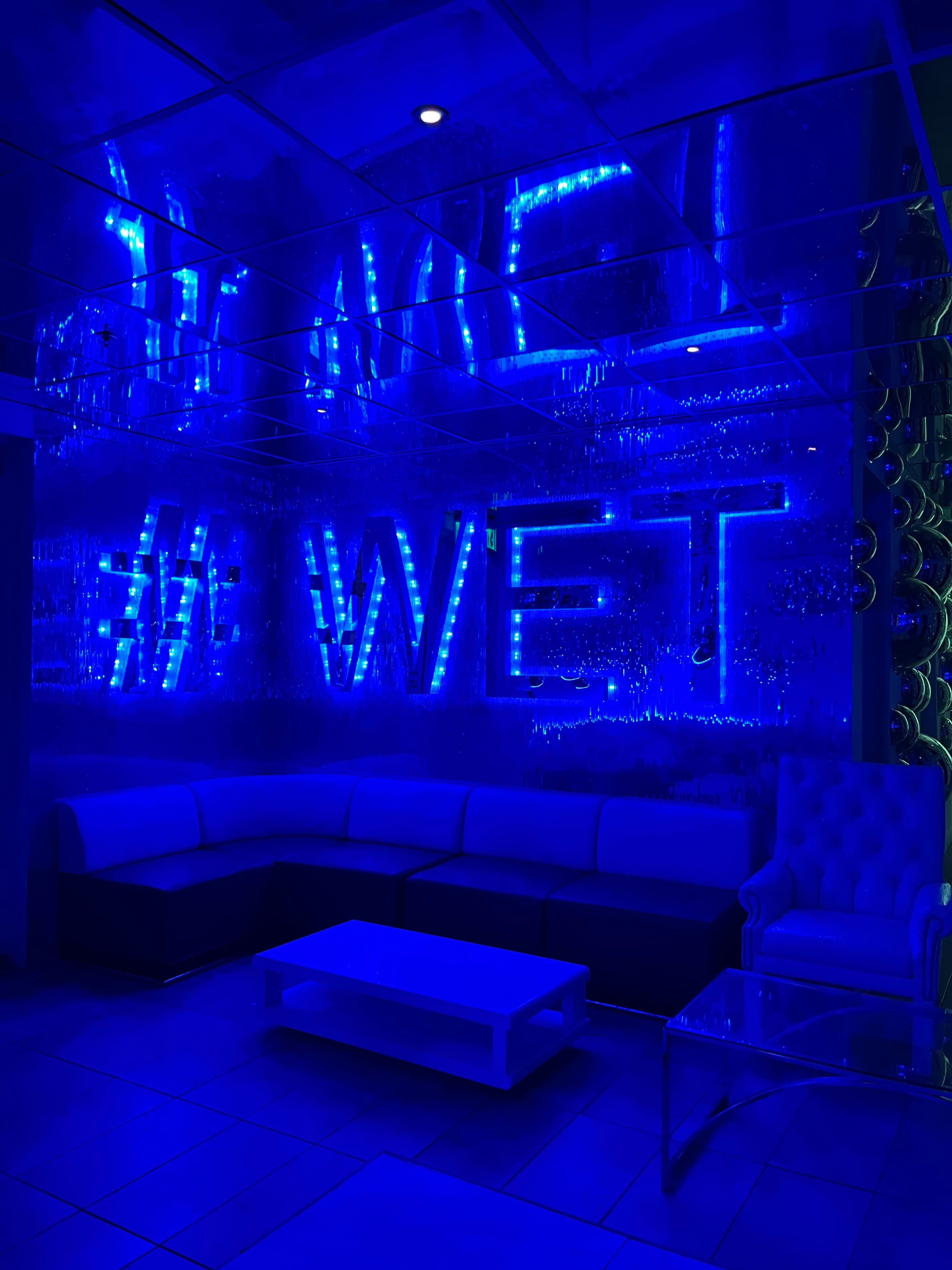 A modern lounge area features a blue-lit wall with the word "WET" and a sleek white couch.