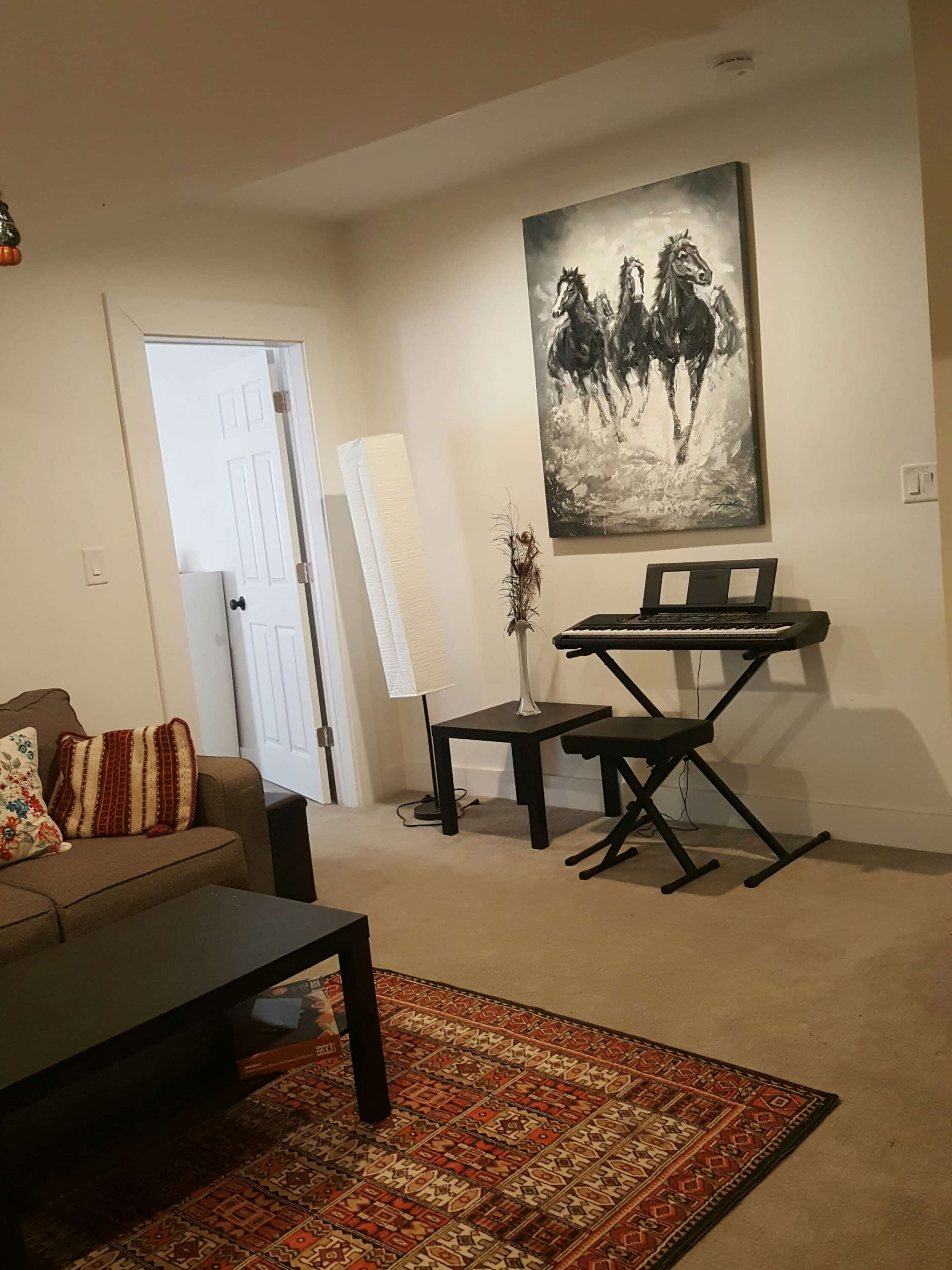 A living room with a gray sofa, a dark coffee table, a keyboard on a stand, and a large painting of three horses on the wall.