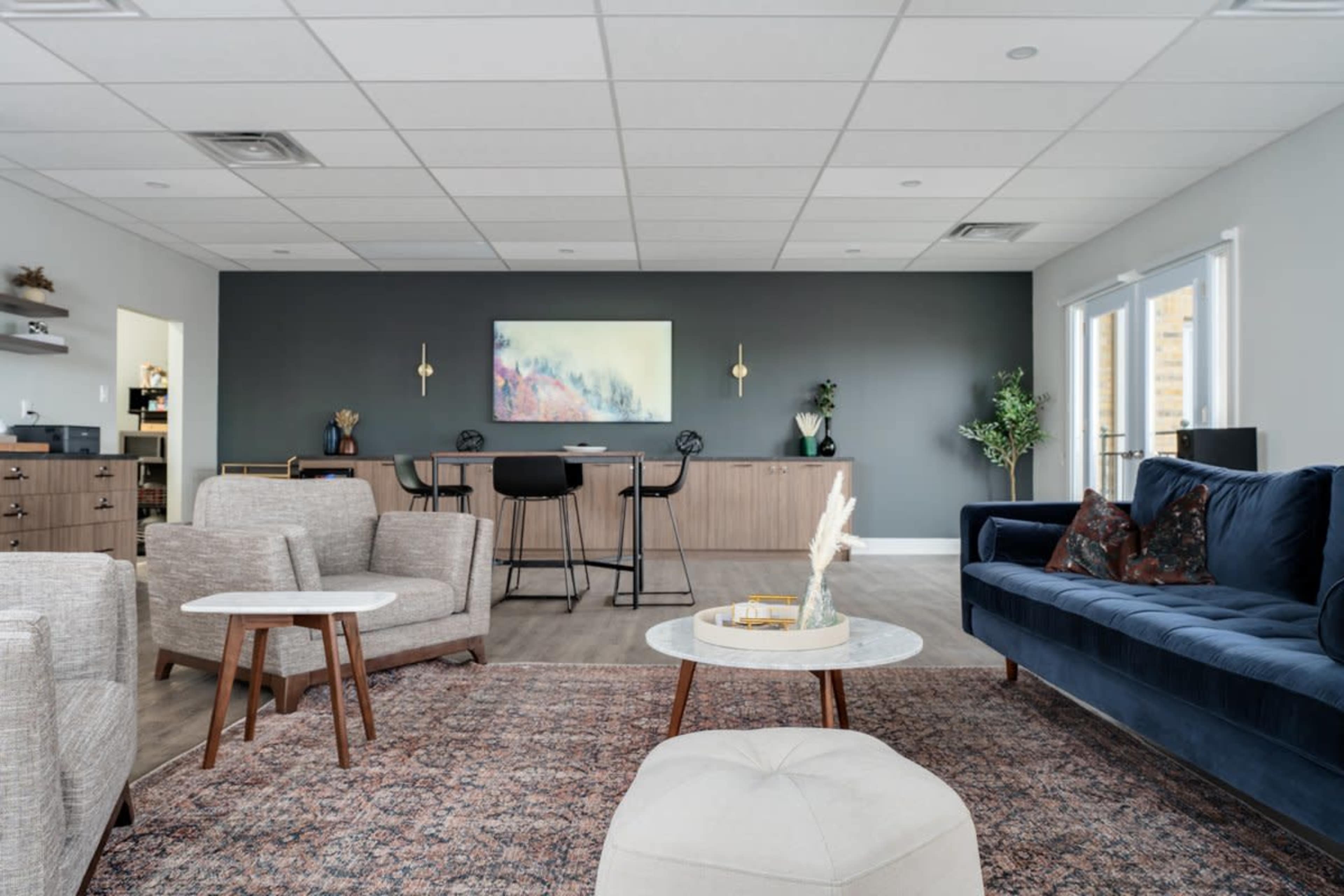 The image shows a modern, minimalist lounge area featuring a dark accent wall, comfortable seating, a coffee table, and a bar counter in the background.