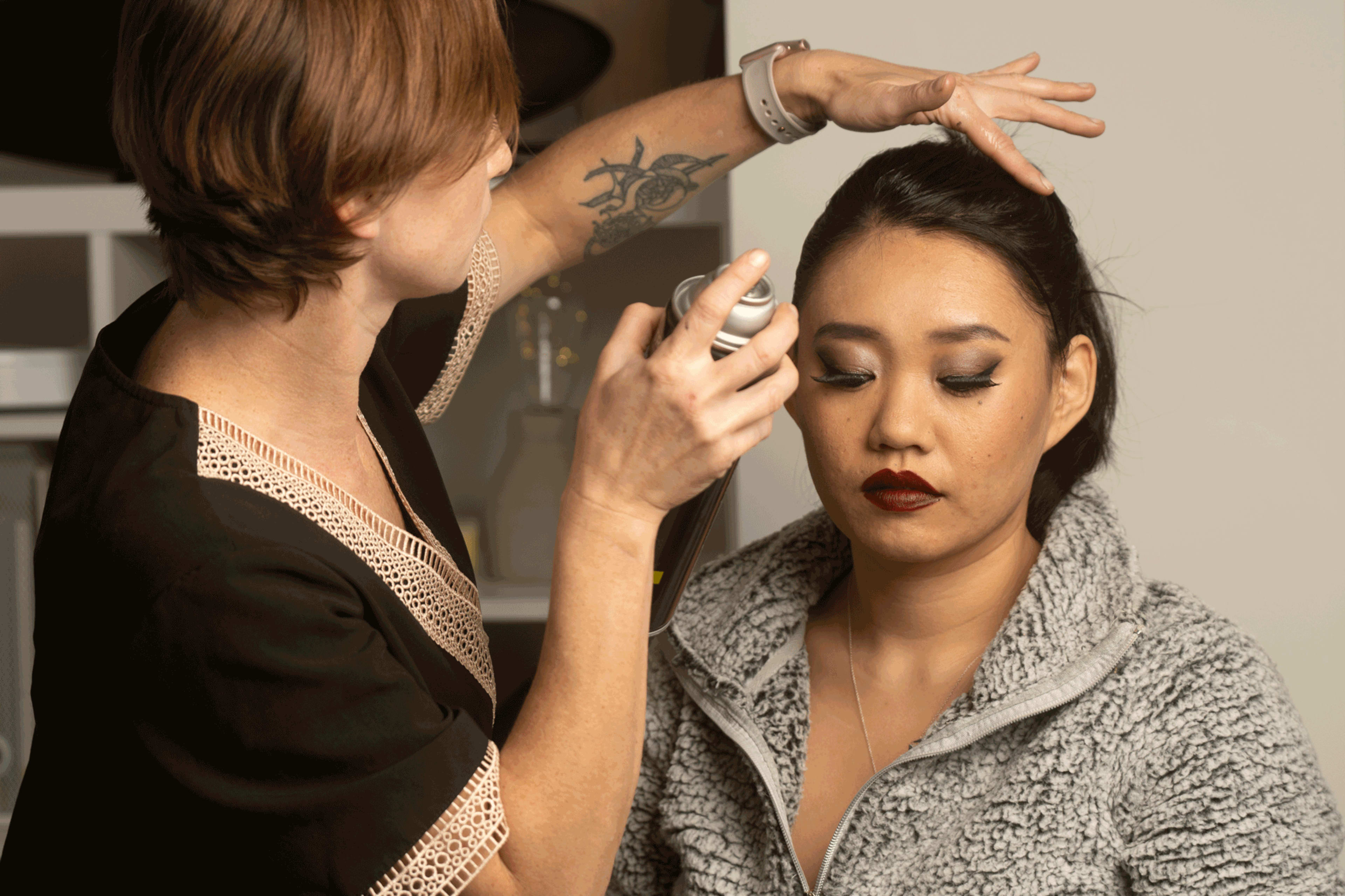 A person is applying hair spray to a woman with styled hair in a beauty setting.
