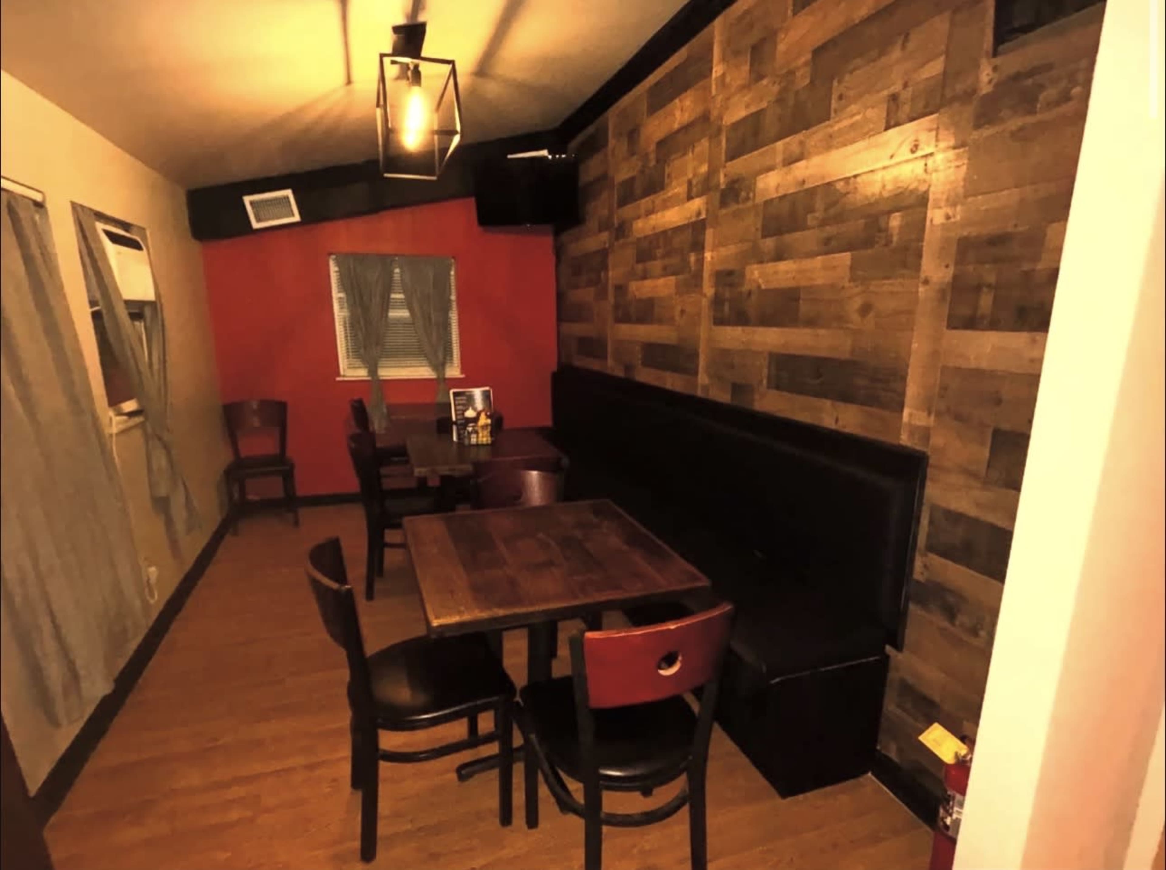 The image shows a small, warmly lit restaurant interior featuring wooden walls, a few wooden tables with chairs, and a plush bench along one side.
