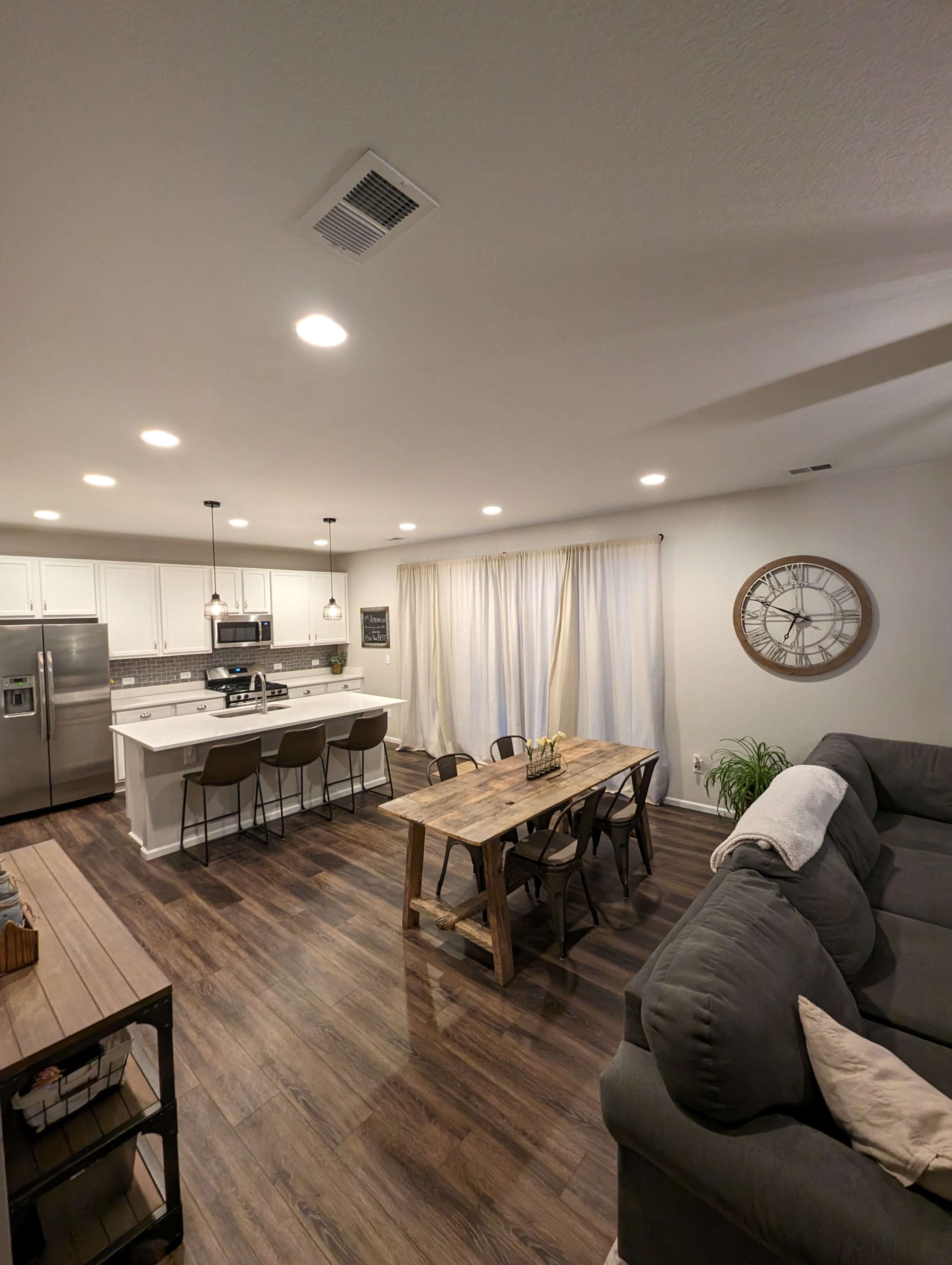 A modern open-concept living space with a kitchen area, a dining table made of wood, and a comfortable sofa, all featuring wooden flooring.