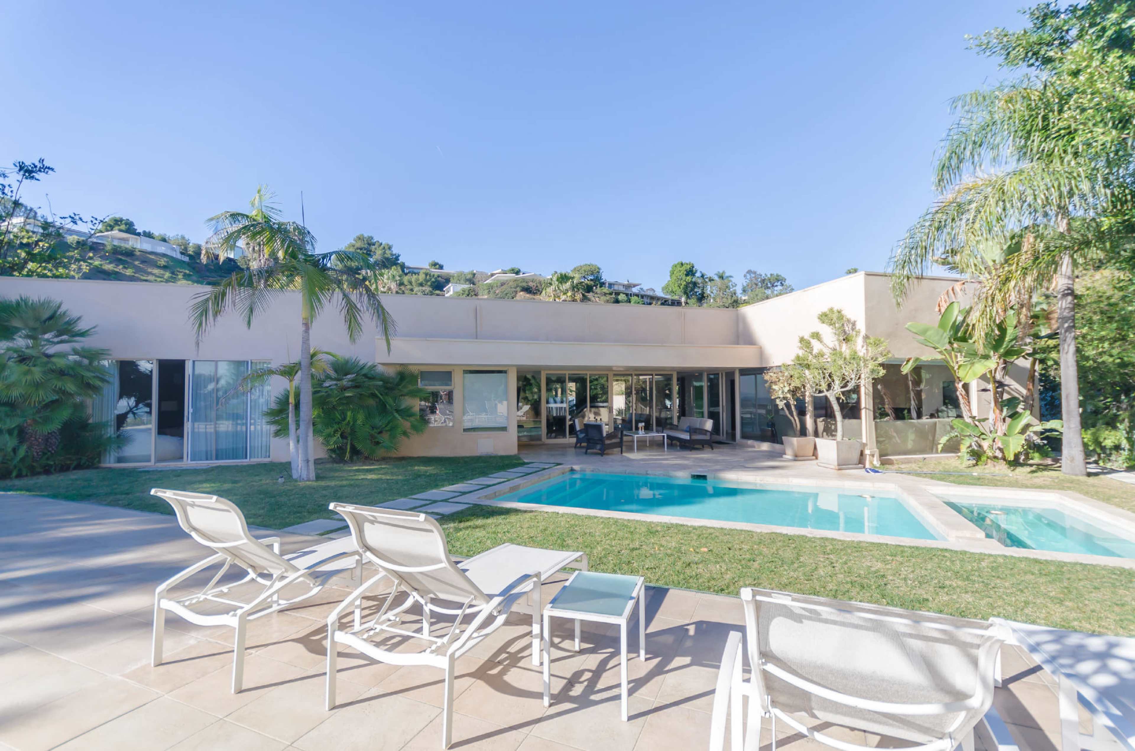 The image shows a modern house with a swimming pool and lounge chairs in a landscaped yard.