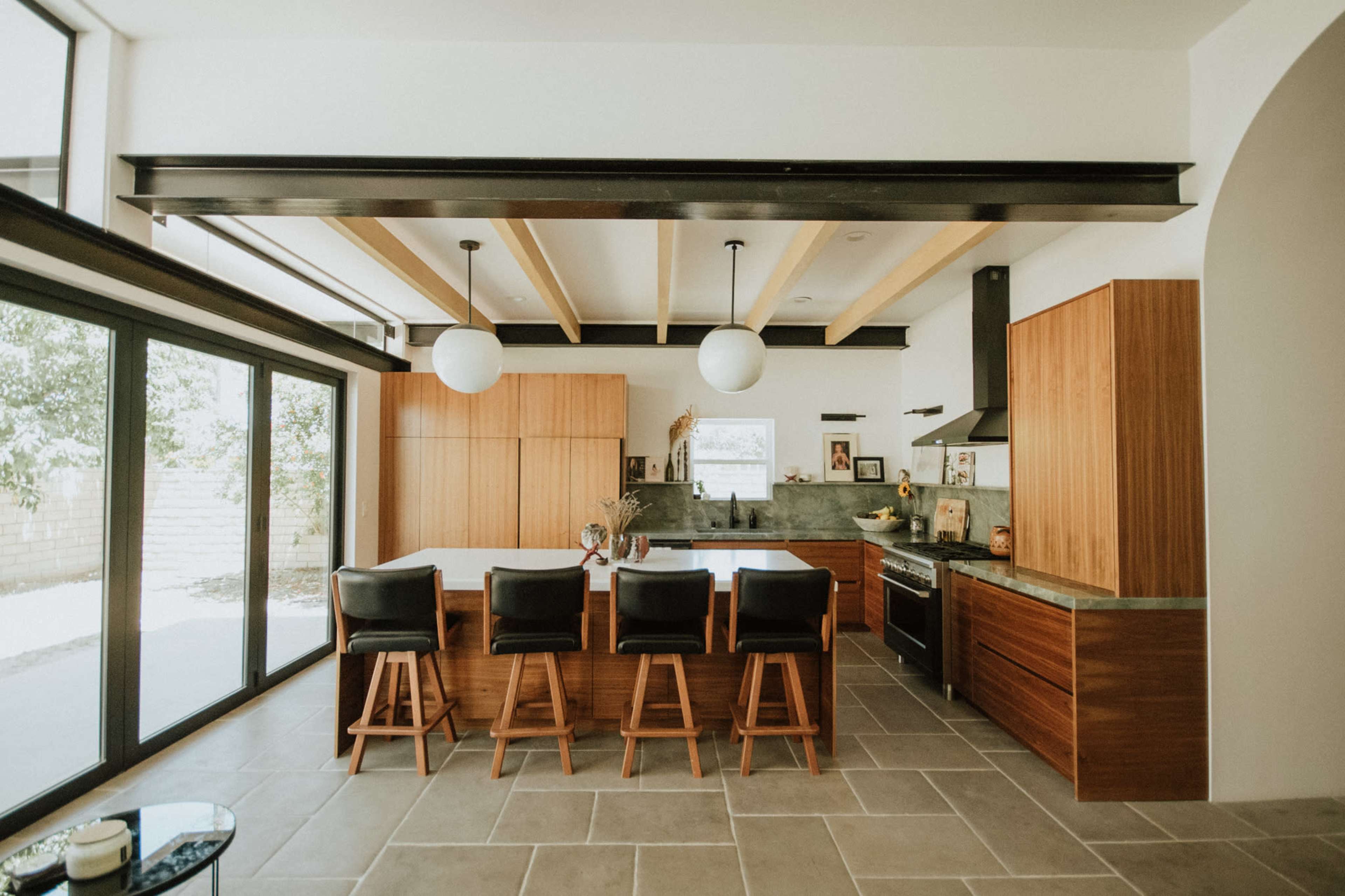 A modern kitchen features wooden cabinetry, a large island with bar seating, and large windows allowing natural light.