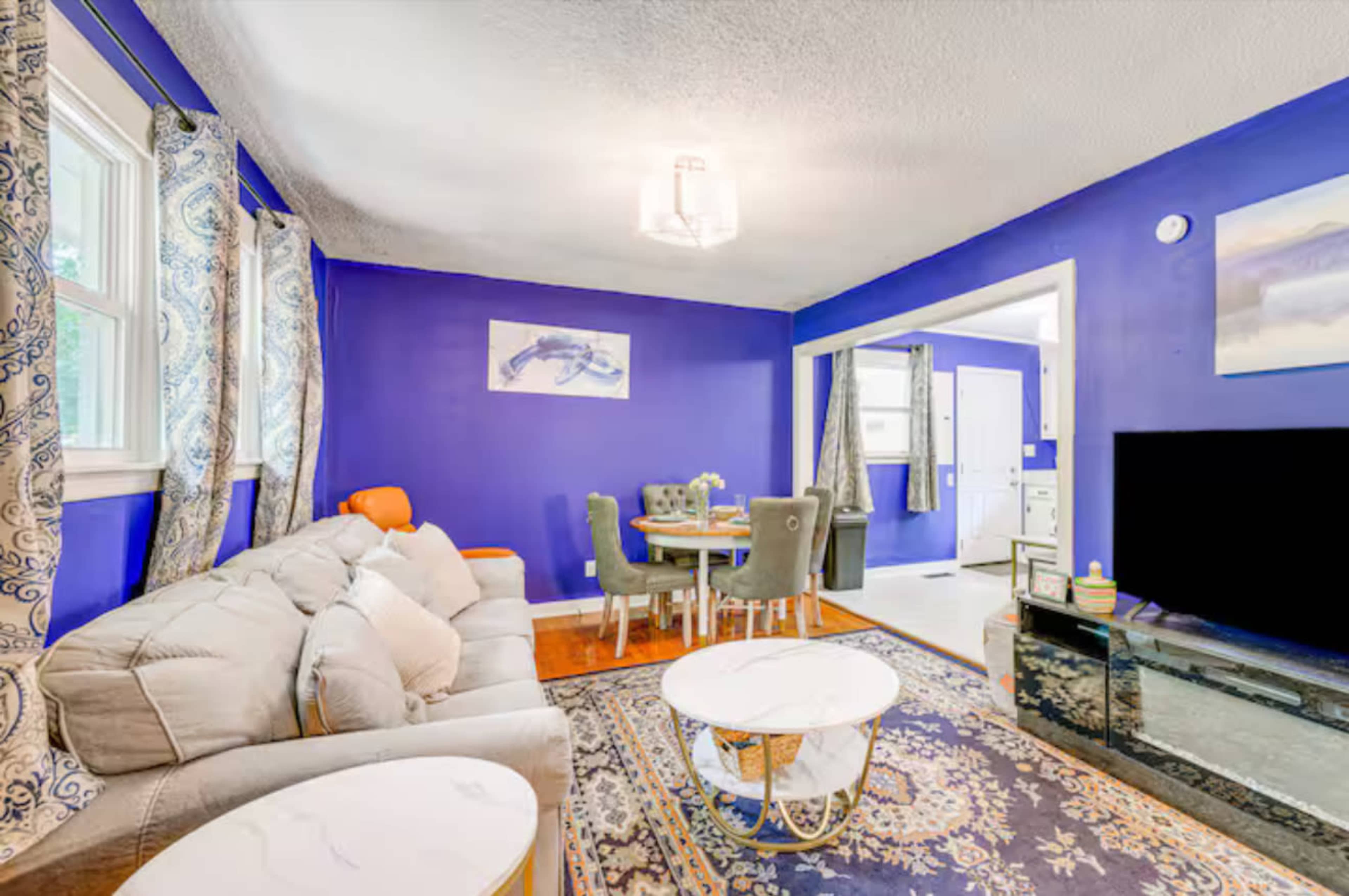 The image shows a living room with a blue accent wall, a gray sofa, two coffee tables, and a dining area visible in the background.