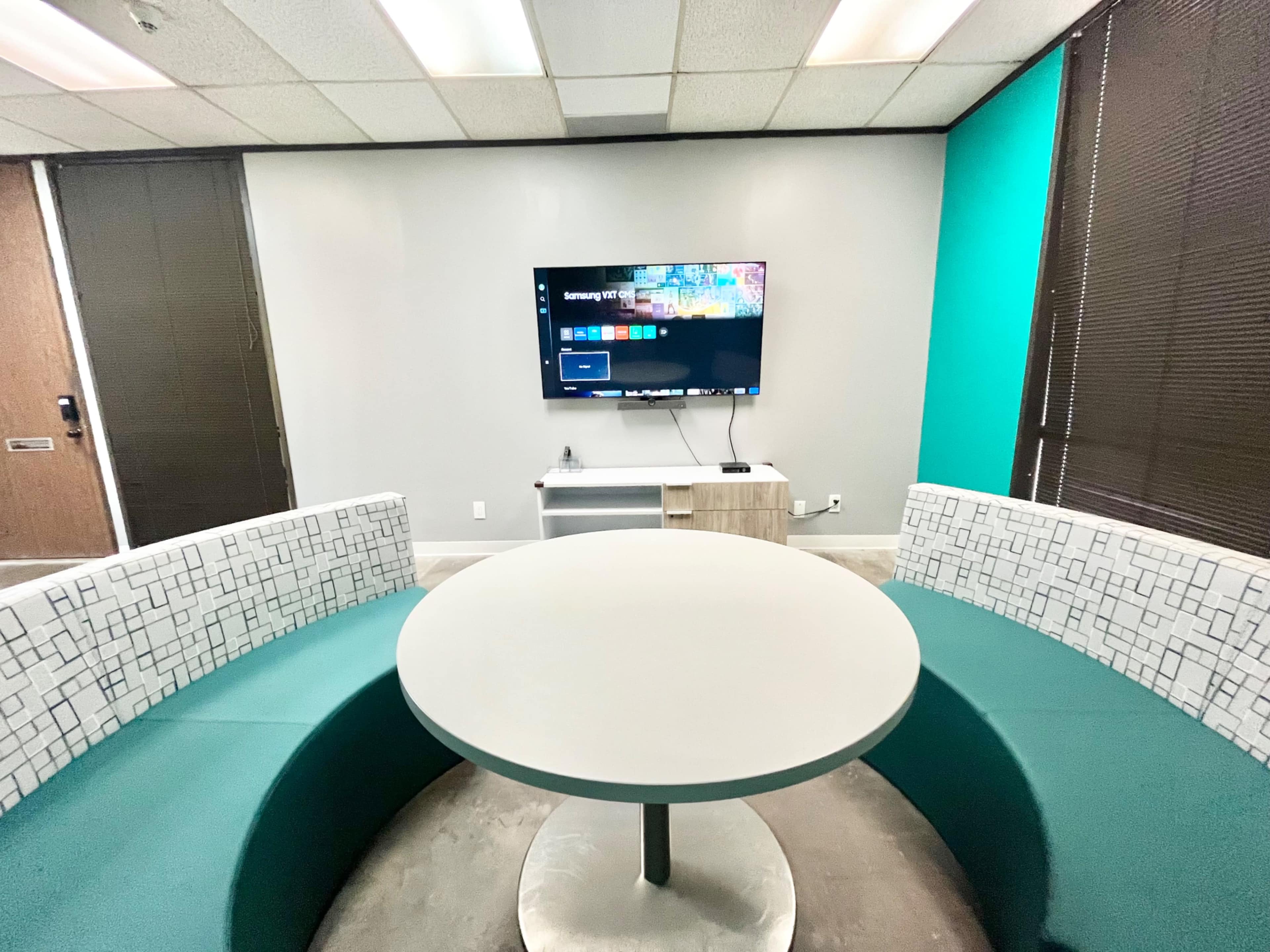 The image shows a modern seating area with a circular table and a semicircular couch, positioned in front of a wall-mounted television.