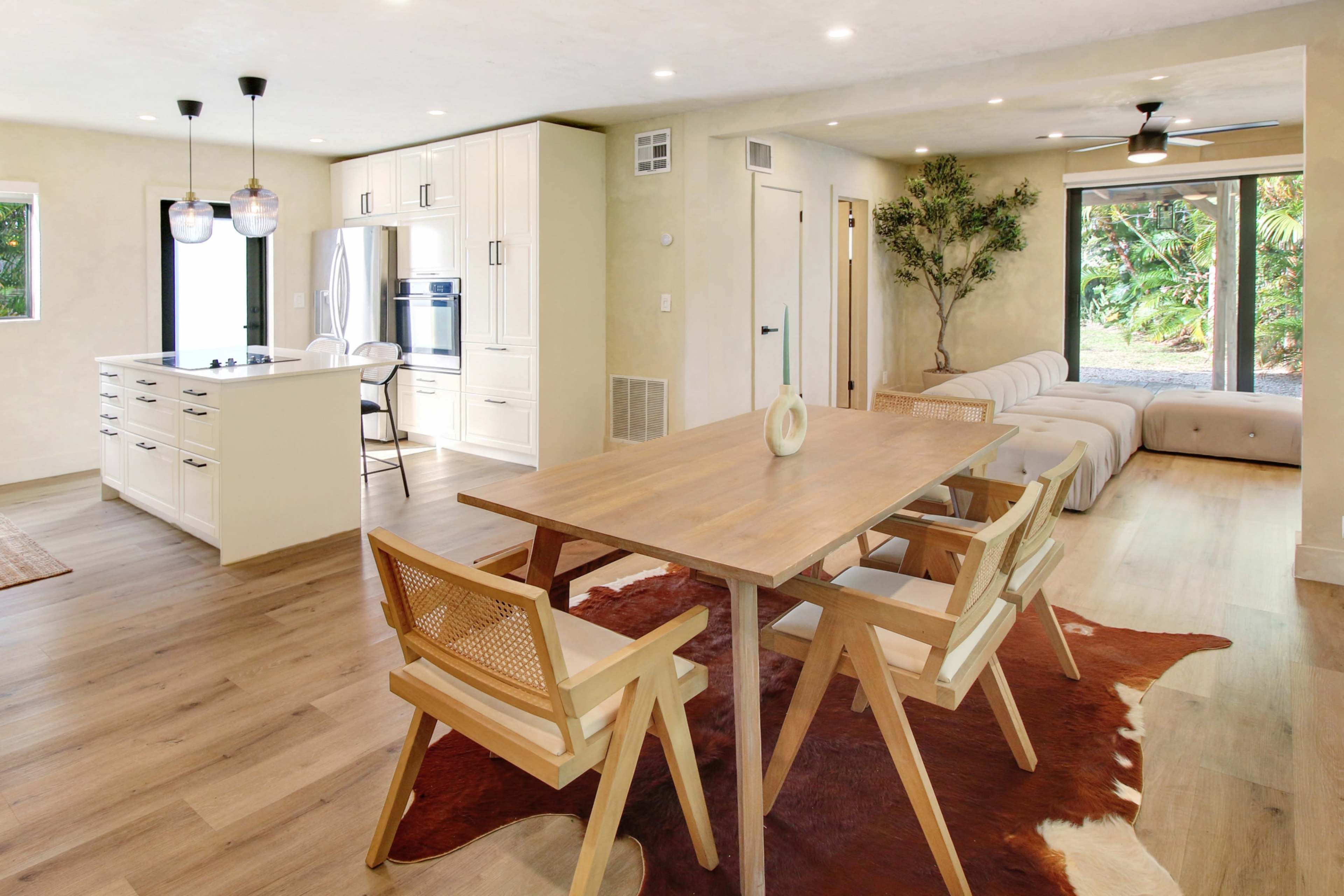 A modern open-concept kitchen and dining area with a wooden table, four chairs, and a light-colored couch in a well-lit space.