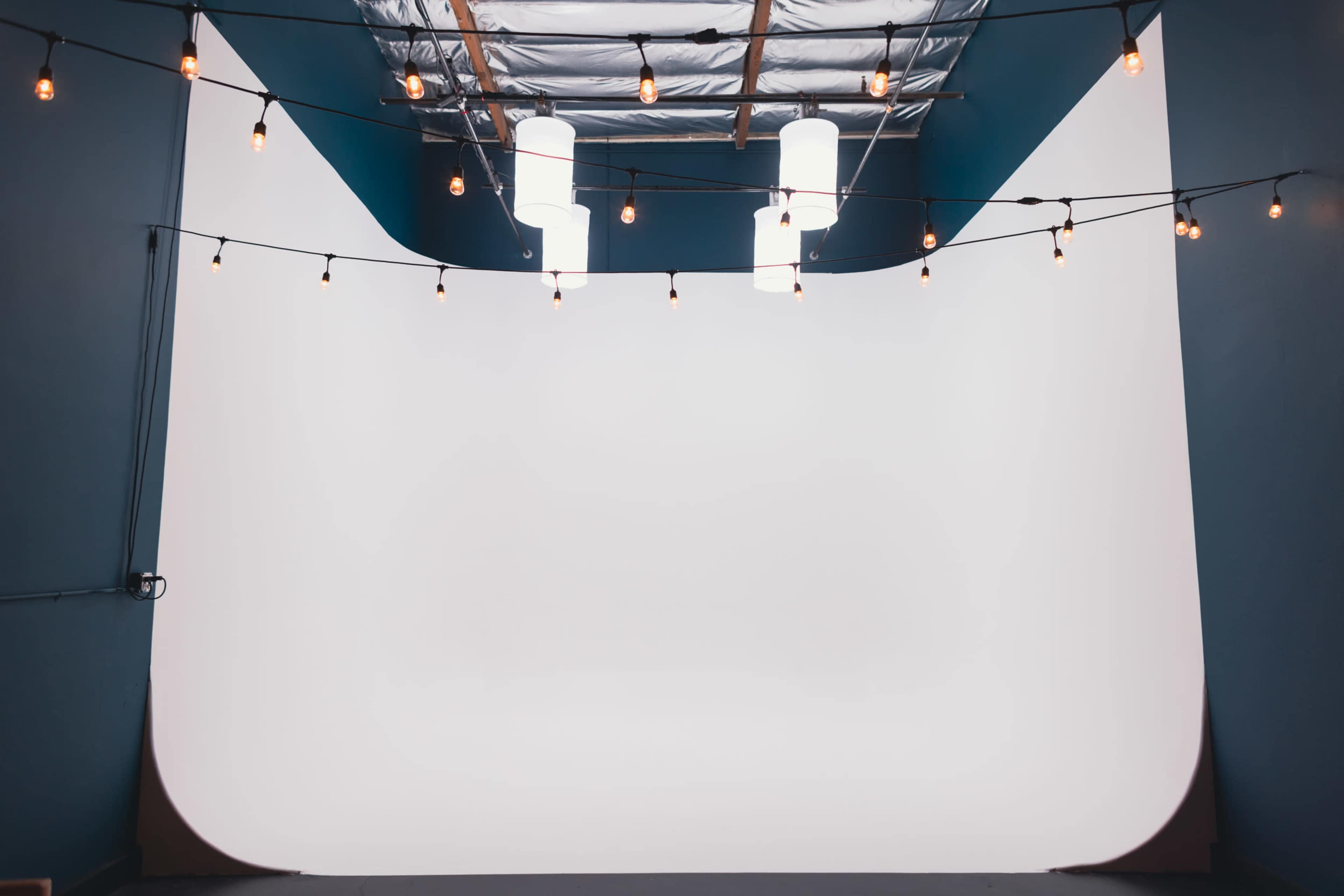 The image shows a spacious photo studio with a curved white backdrop and pendant lights hanging from the ceiling.