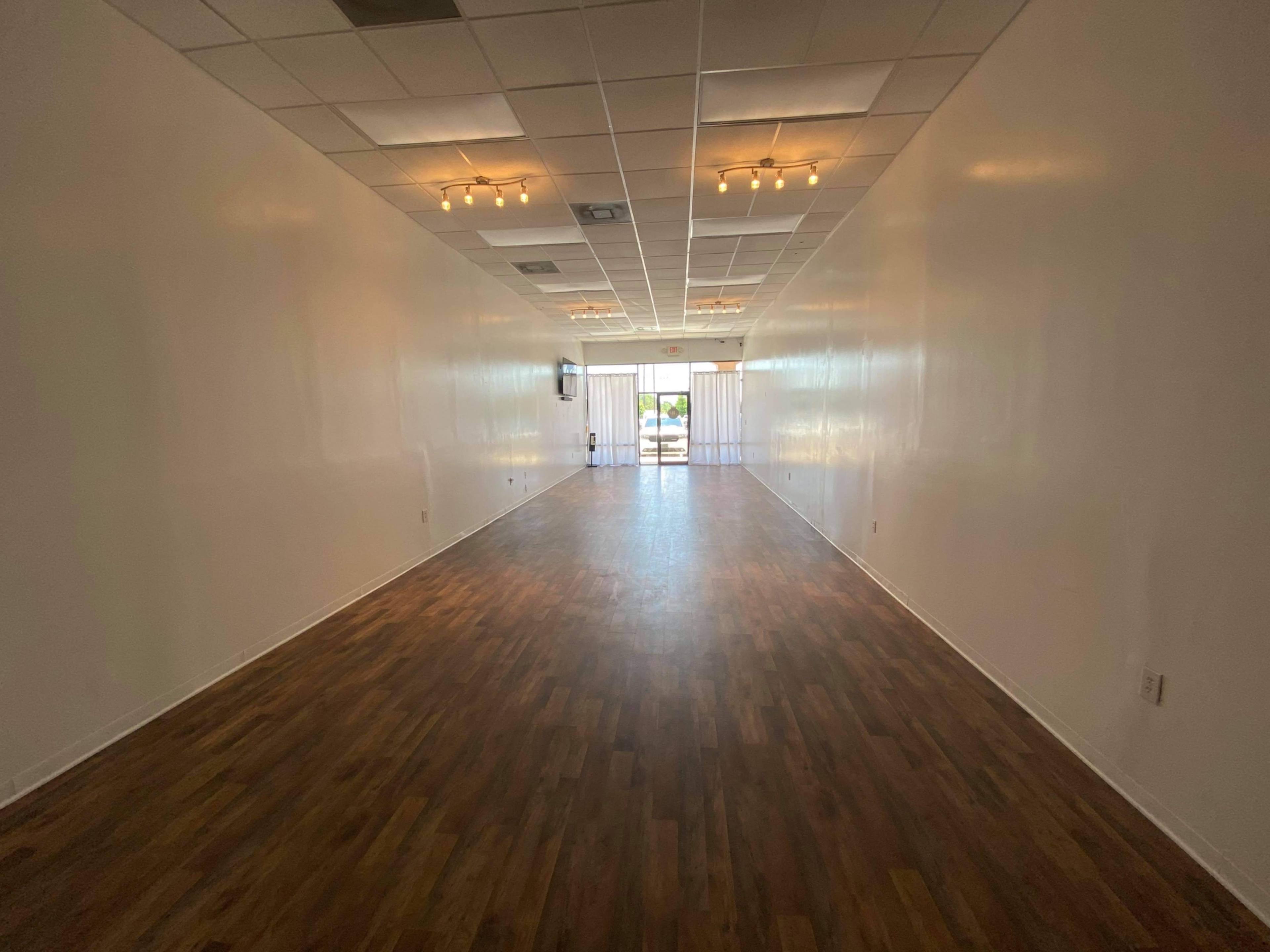 A spacious, empty interior room with wooden flooring and large windows at one end.