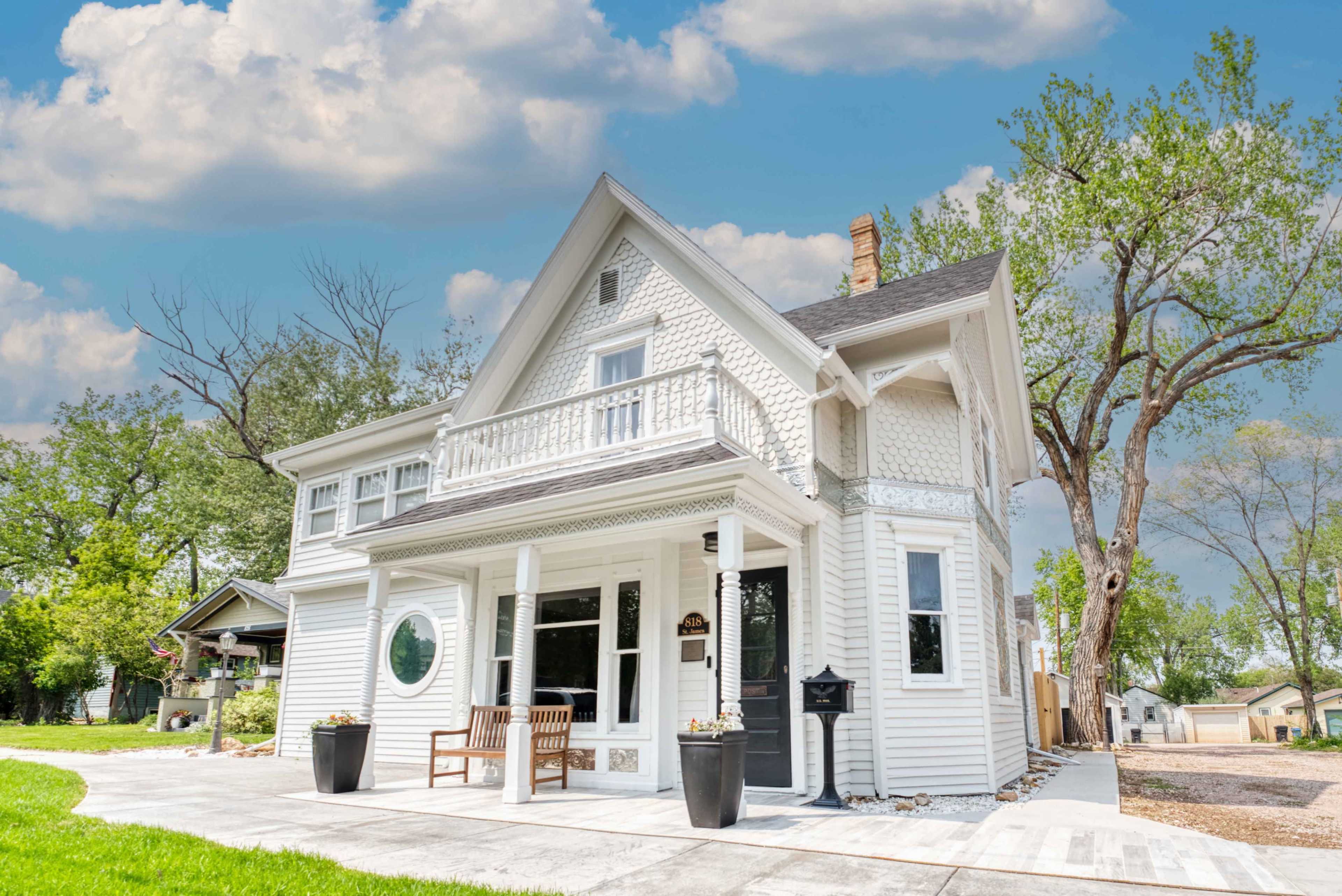A white Victorian-style house with intricate details, a front porch, and large windows against a backdrop of a blue sky and trees.