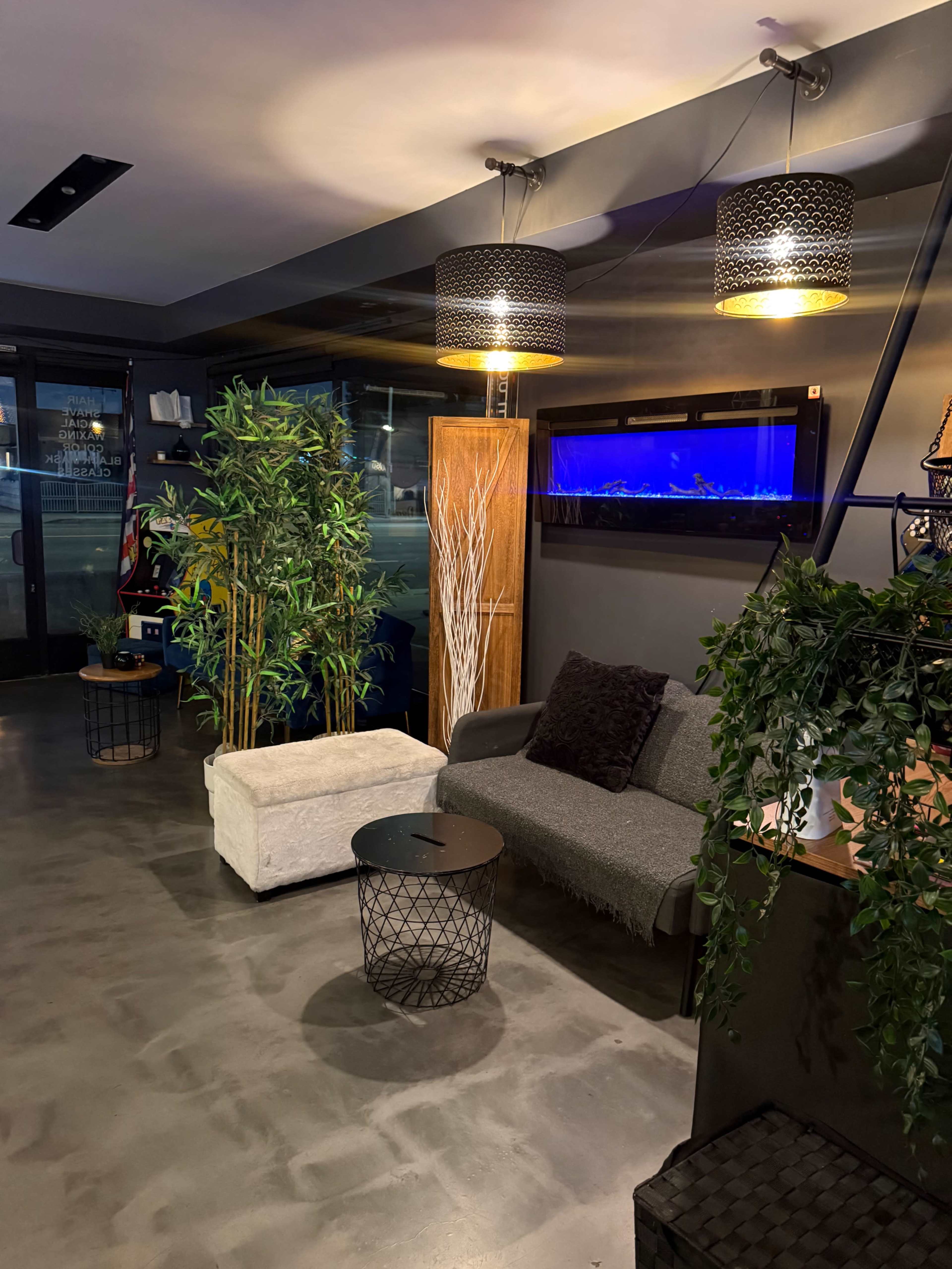 The image shows a modern lobby area featuring a gray sofa, a small round table, decorative plants, and an illuminated aquarium against a dark wall.
