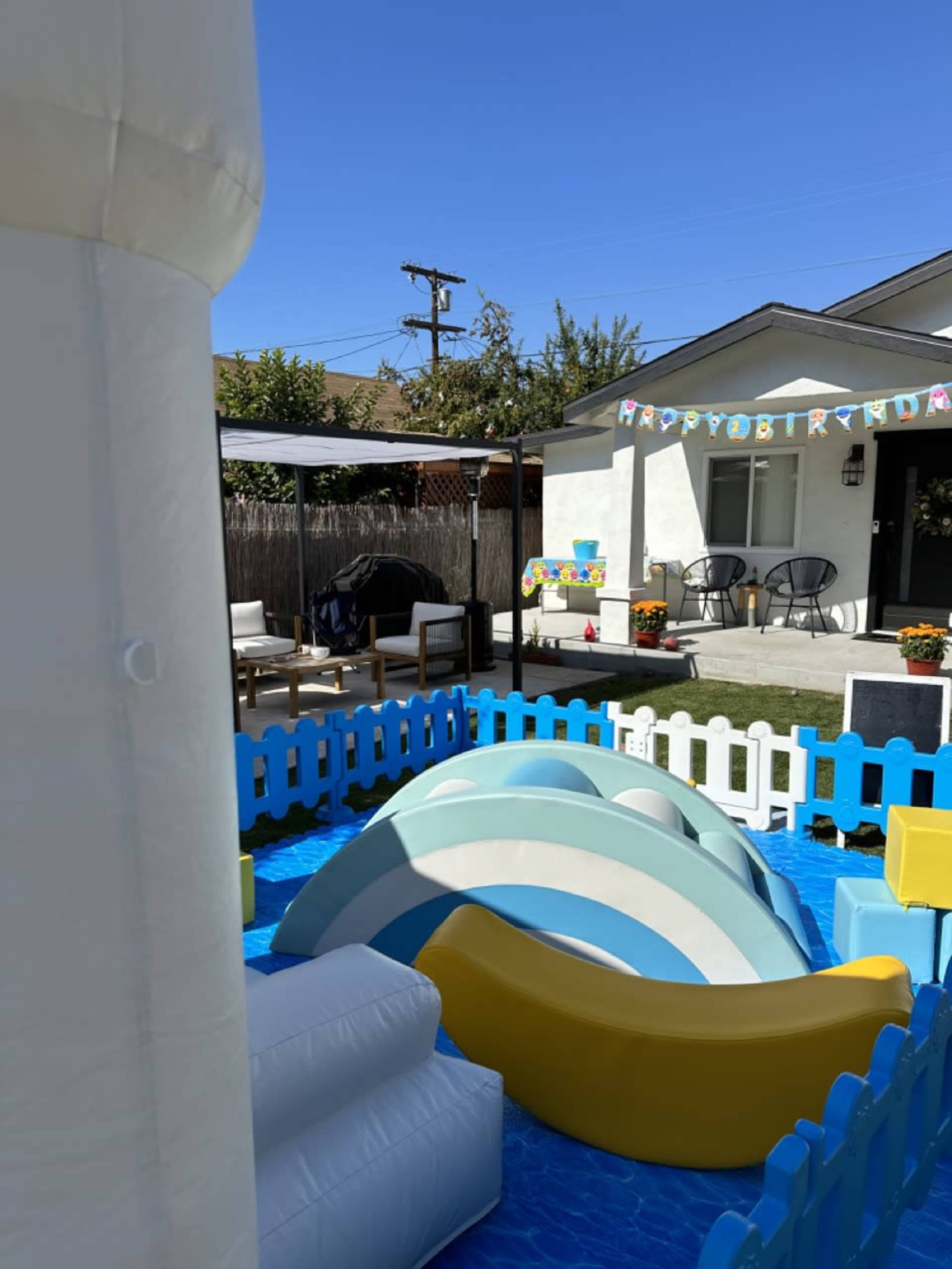 A colorful inflatable play area with slides and a pool is set up in a backyard, featuring decorations for a birthday celebration.