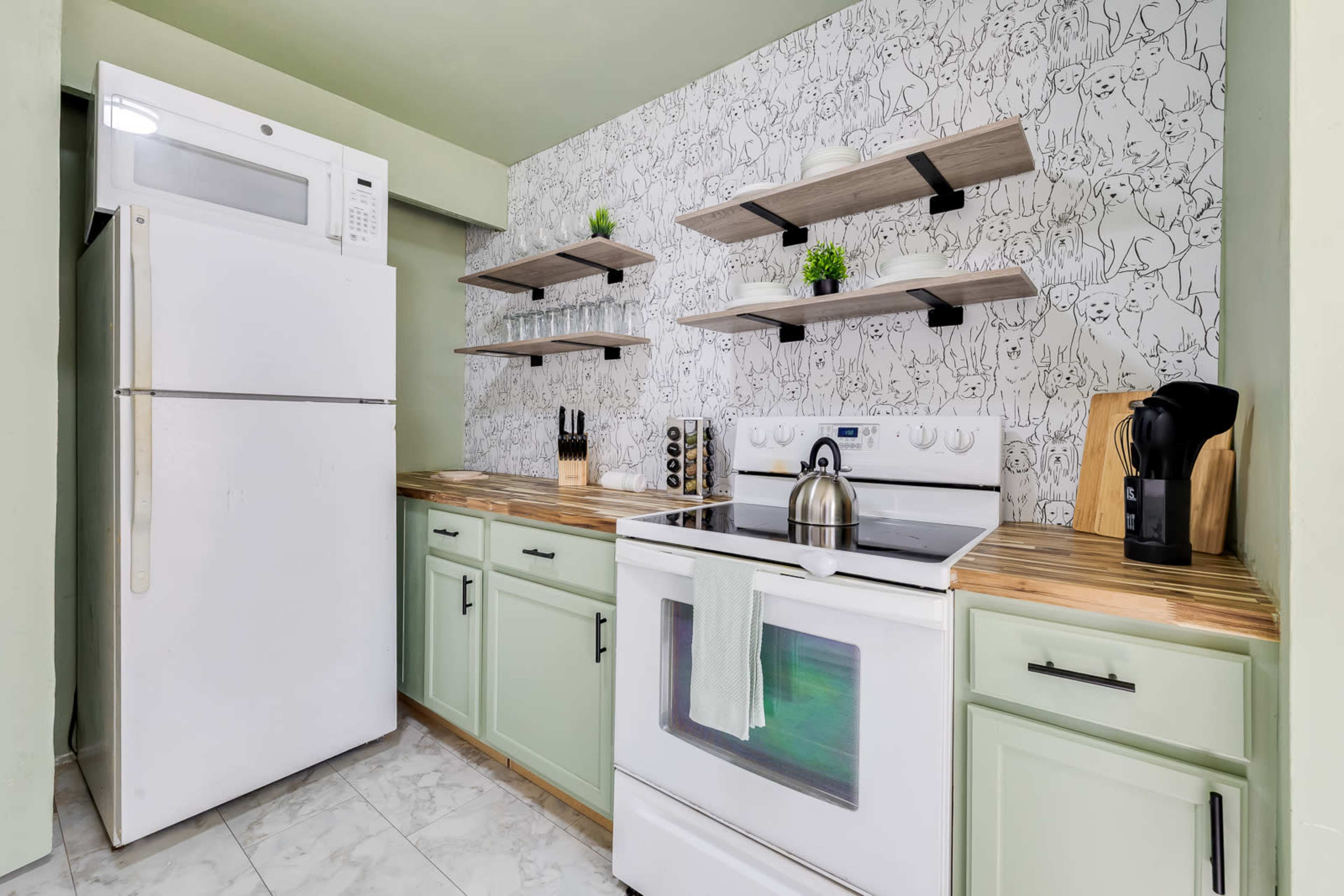 The image shows a kitchen featuring a white refrigerator, a white stove with an oven, wood countertops, and open shelves displaying green plants against a patterned wall.