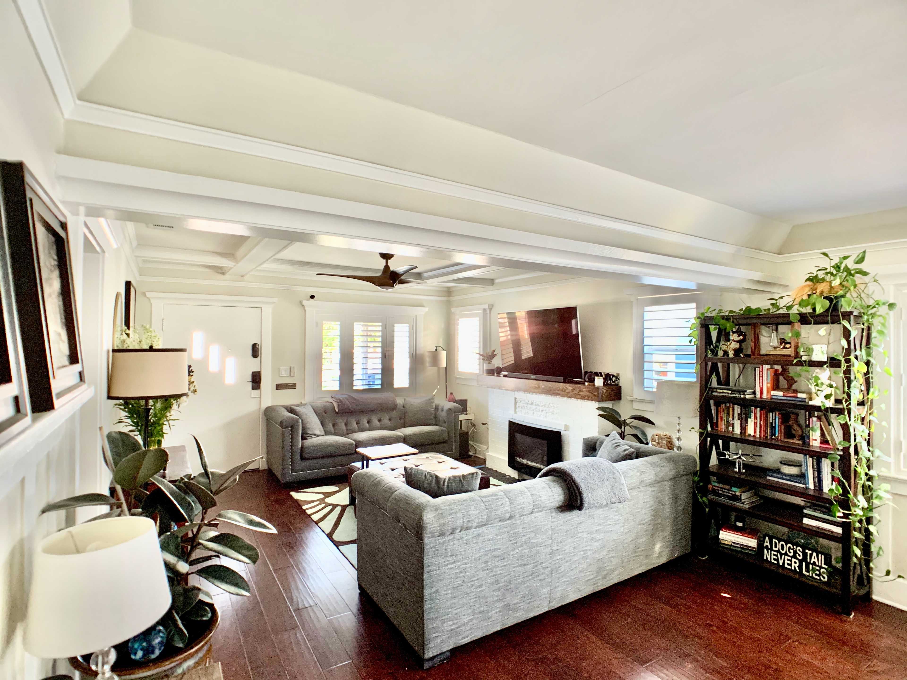 A living room with gray sofas, a coffee table, and a bookshelf, featuring natural light and wooden flooring.