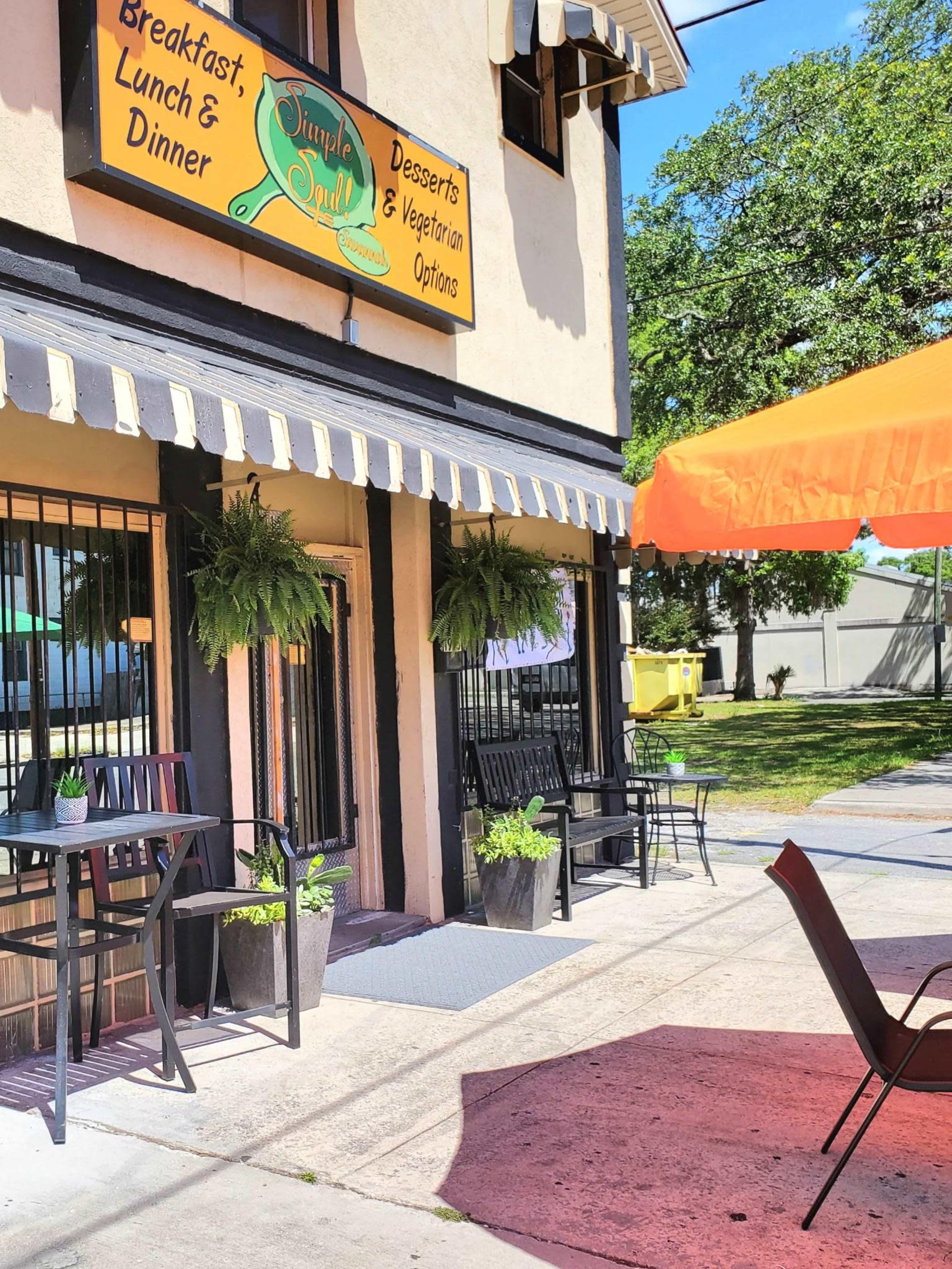 A quaint restaurant with signage advertising breakfast, lunch, dinner, desserts, and vegetarian options, featuring outdoor seating and potted plants.