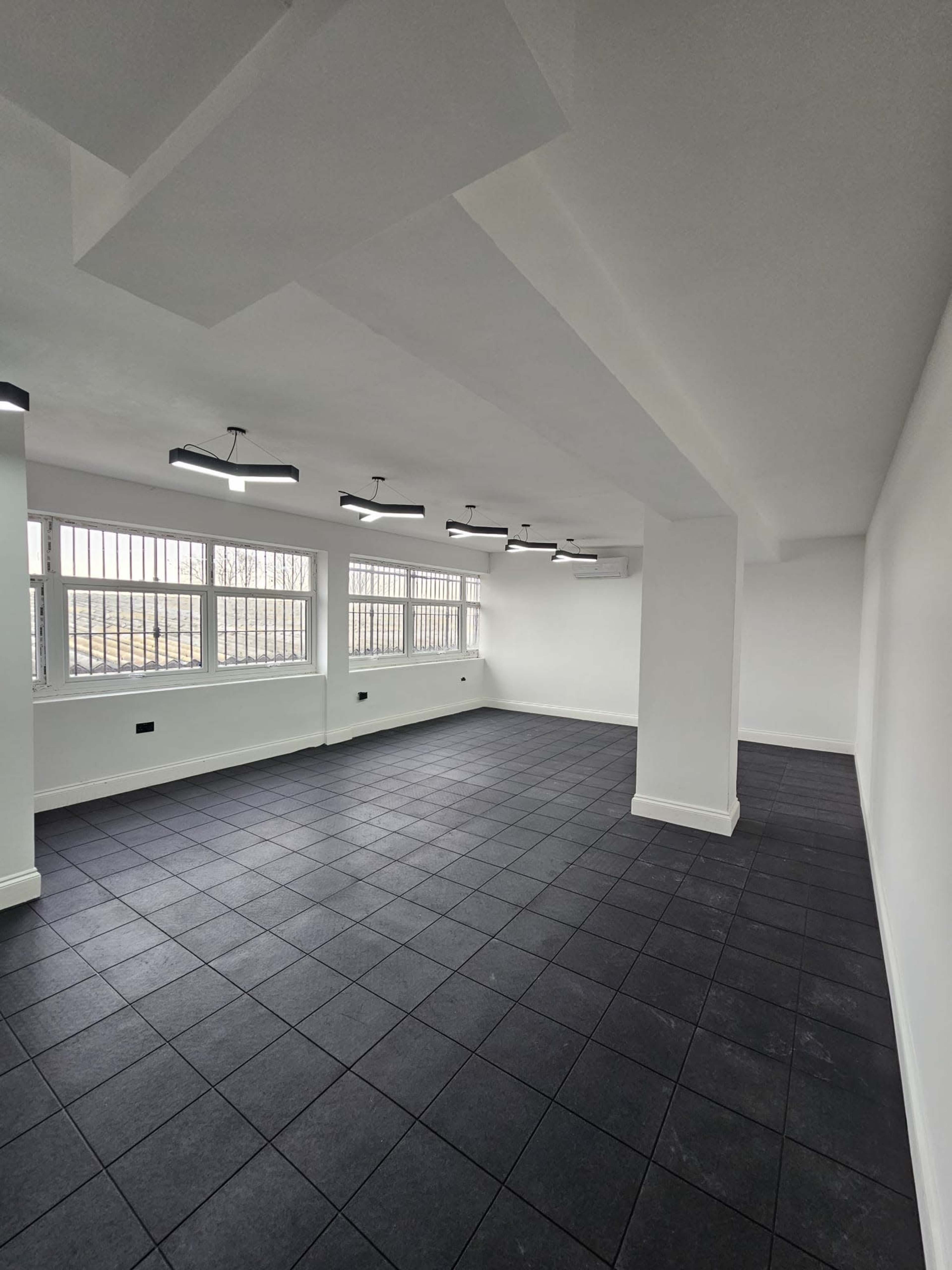 The image shows a vacant room with black tiled flooring, white walls, and several overhead lights illuminating the space.