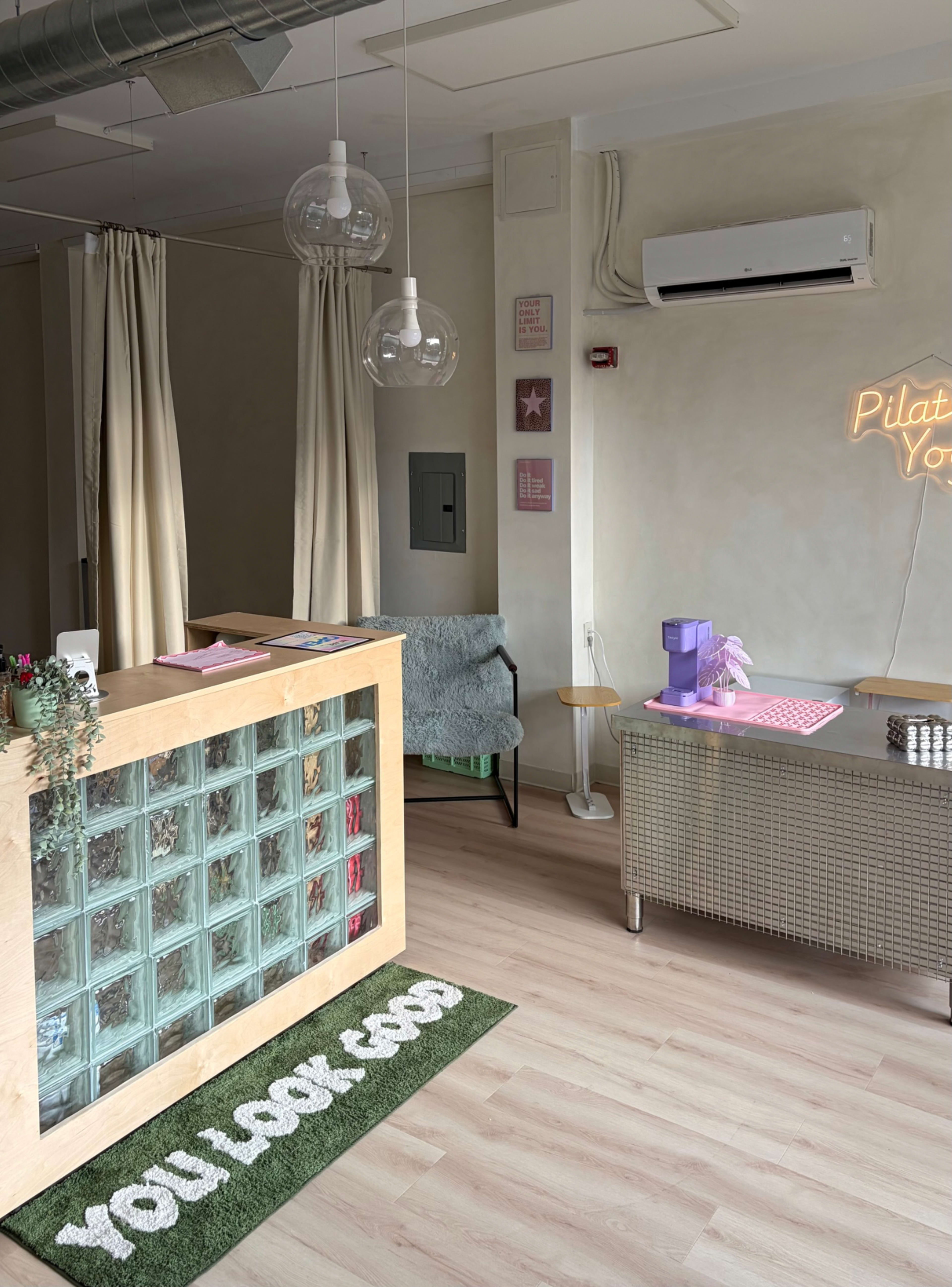 The image shows a bright reception area with a glass block counter, a green chair, and a neon sign that reads "YOU LOOK GOOD."