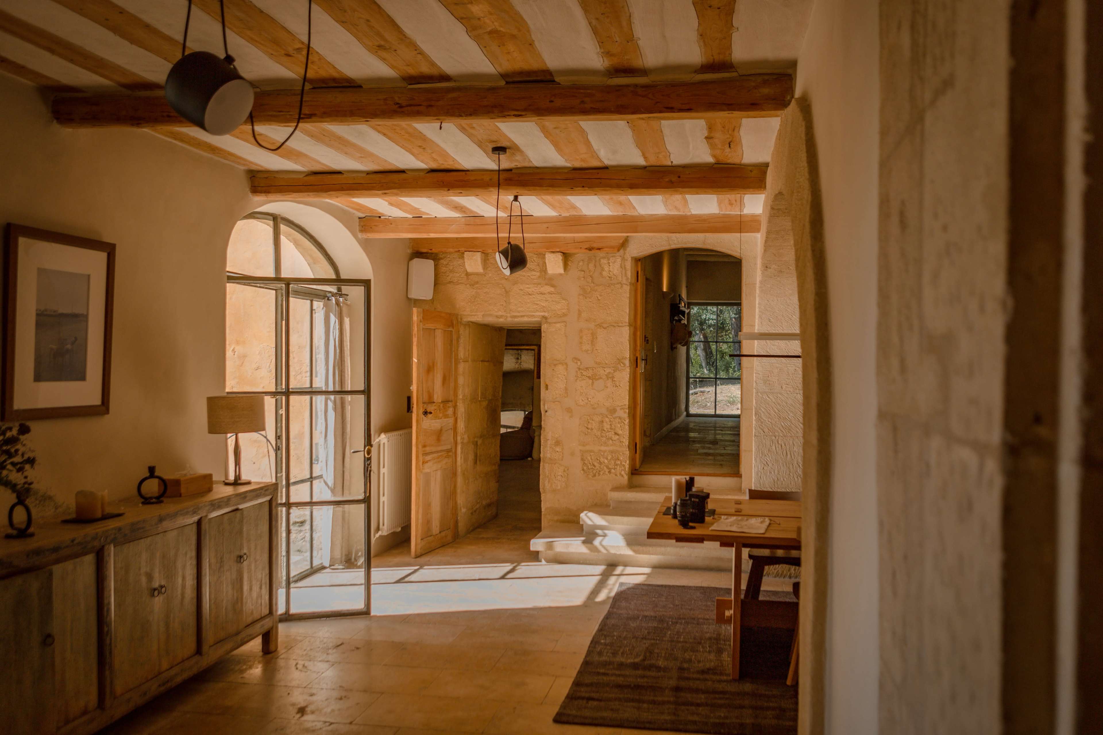 A spacious hallway features wooden beams, stone walls, and an open door leading to a bright interior space.