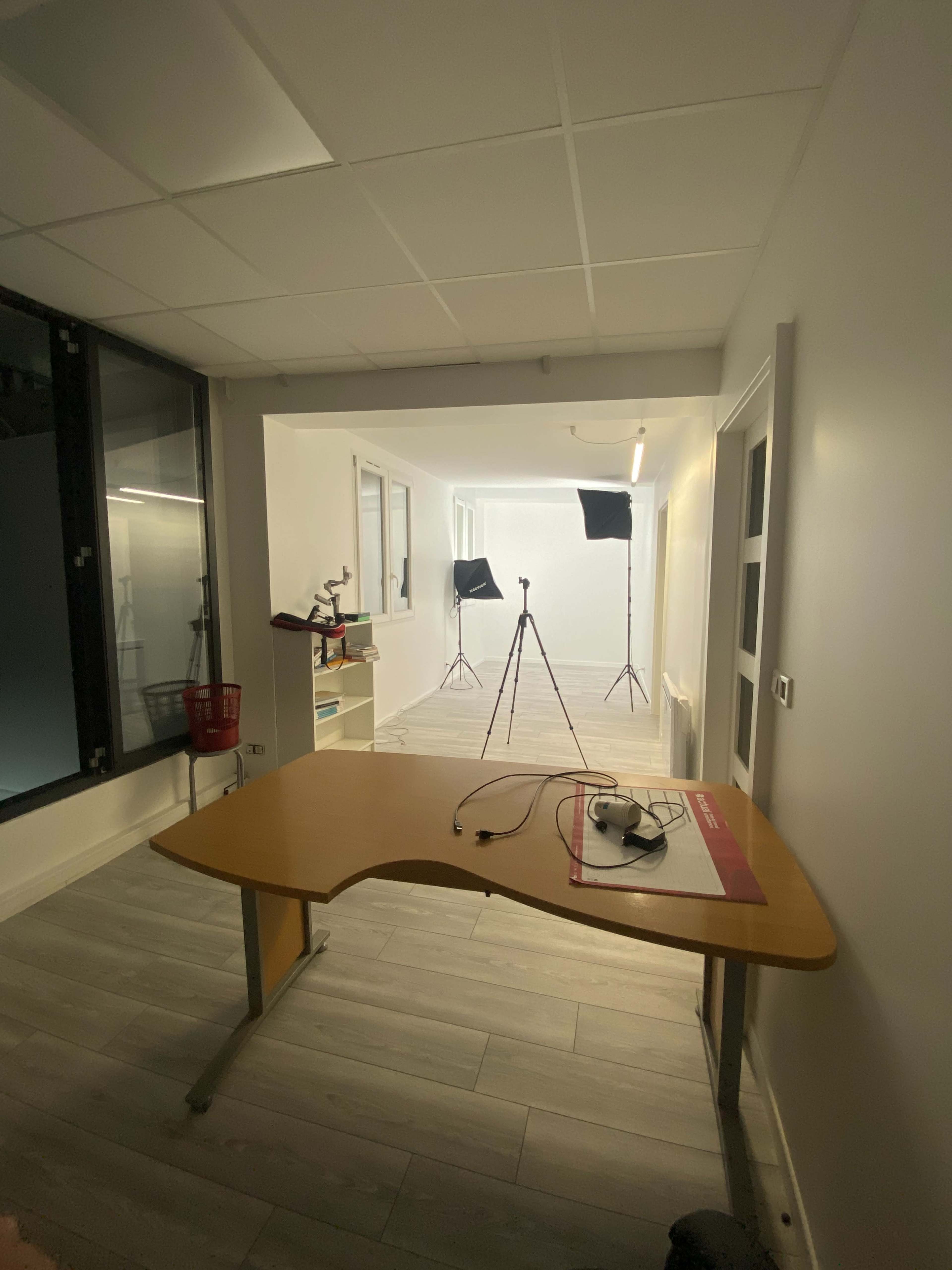 The image shows a bright, empty room with a table in the foreground and two lighting stands set up in the background.