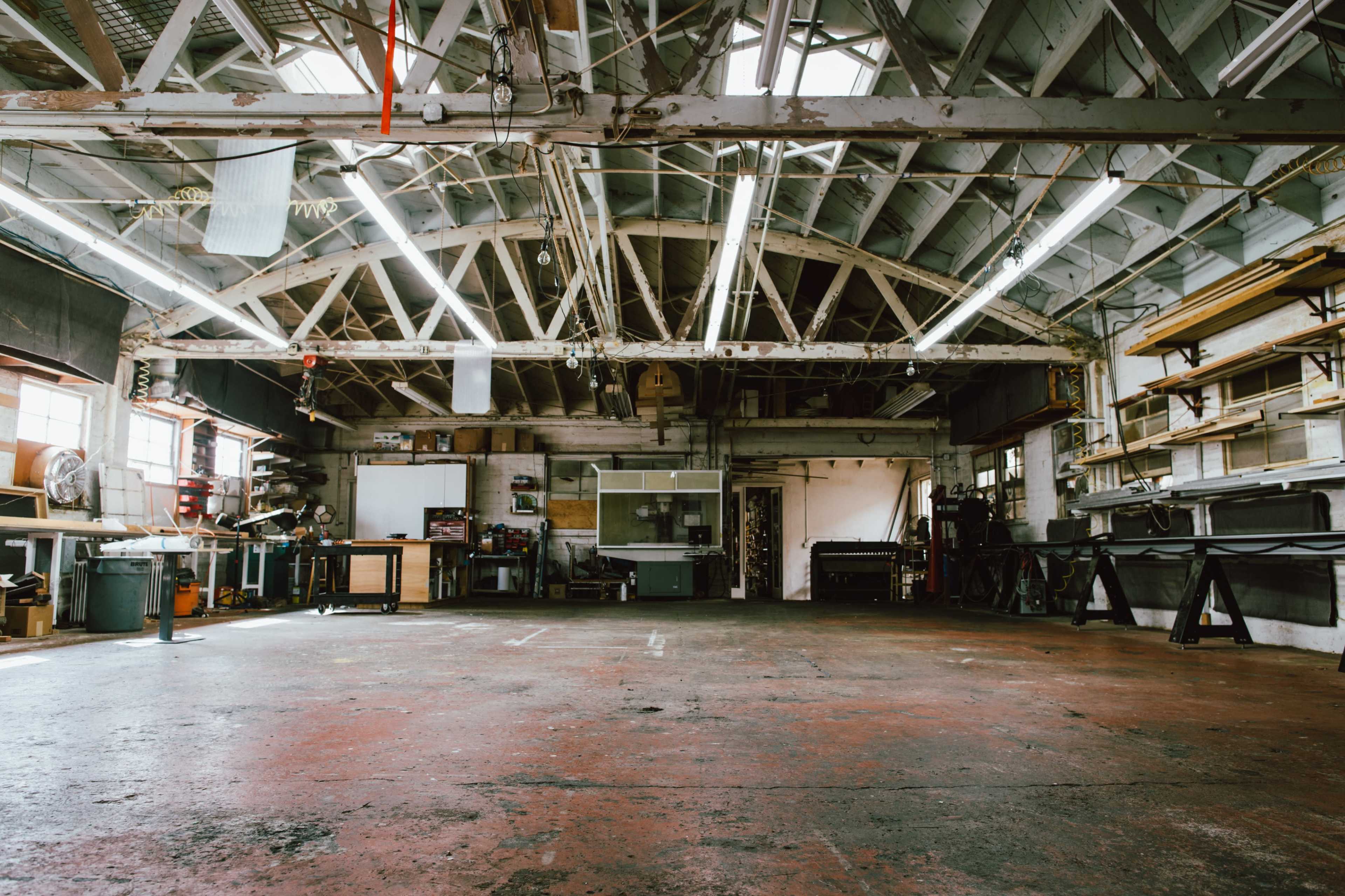 A spacious workshop with high ceilings, exposed beams, and various tools and equipment arranged along the walls.
