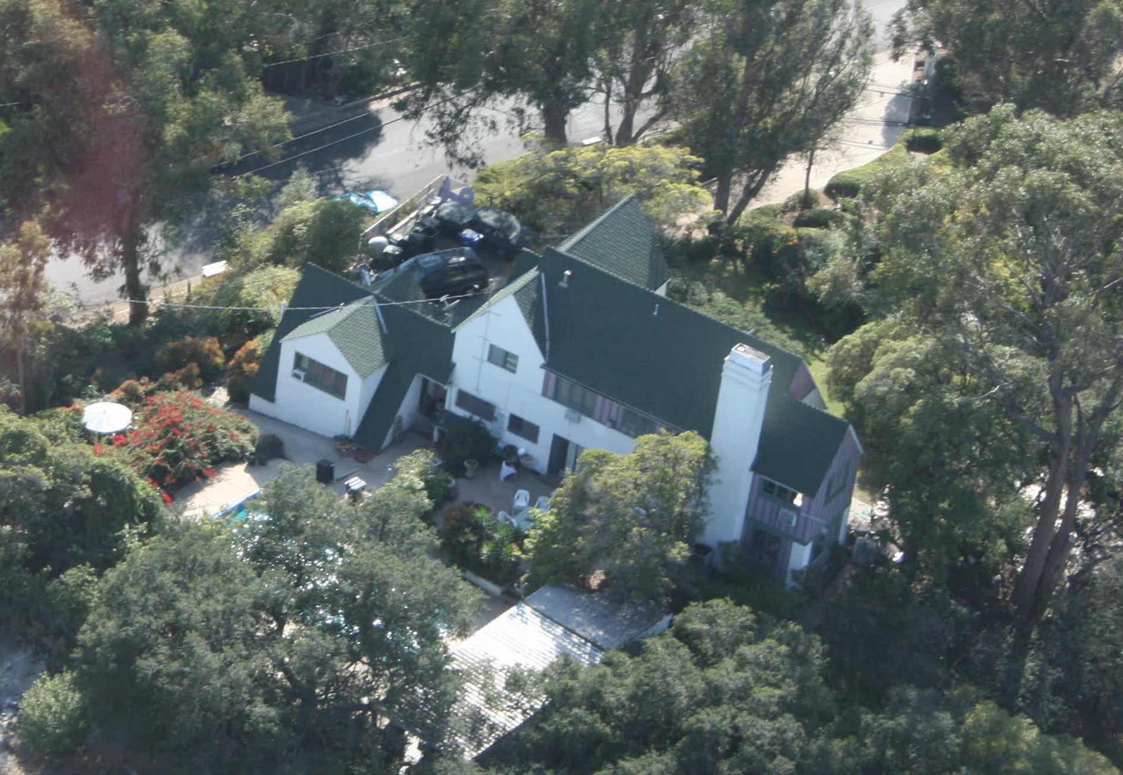 An aerial view of a large house with a green roof surrounded by trees and a neatly landscaped yard.
