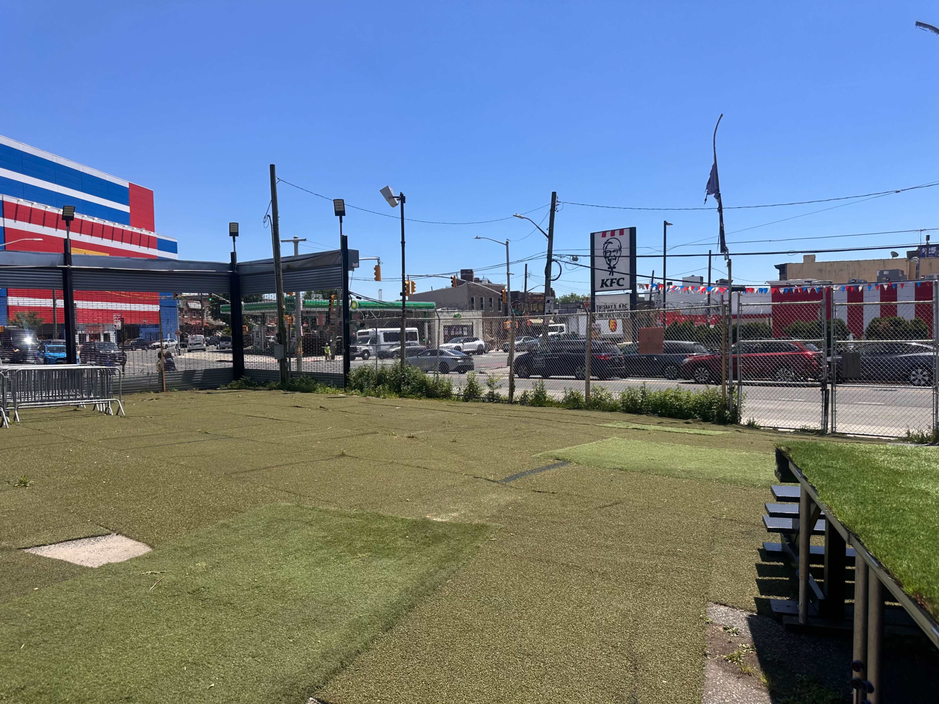 The image shows a fenced outdoor area with artificial grass, a seating structure, and a KFC sign in the background.