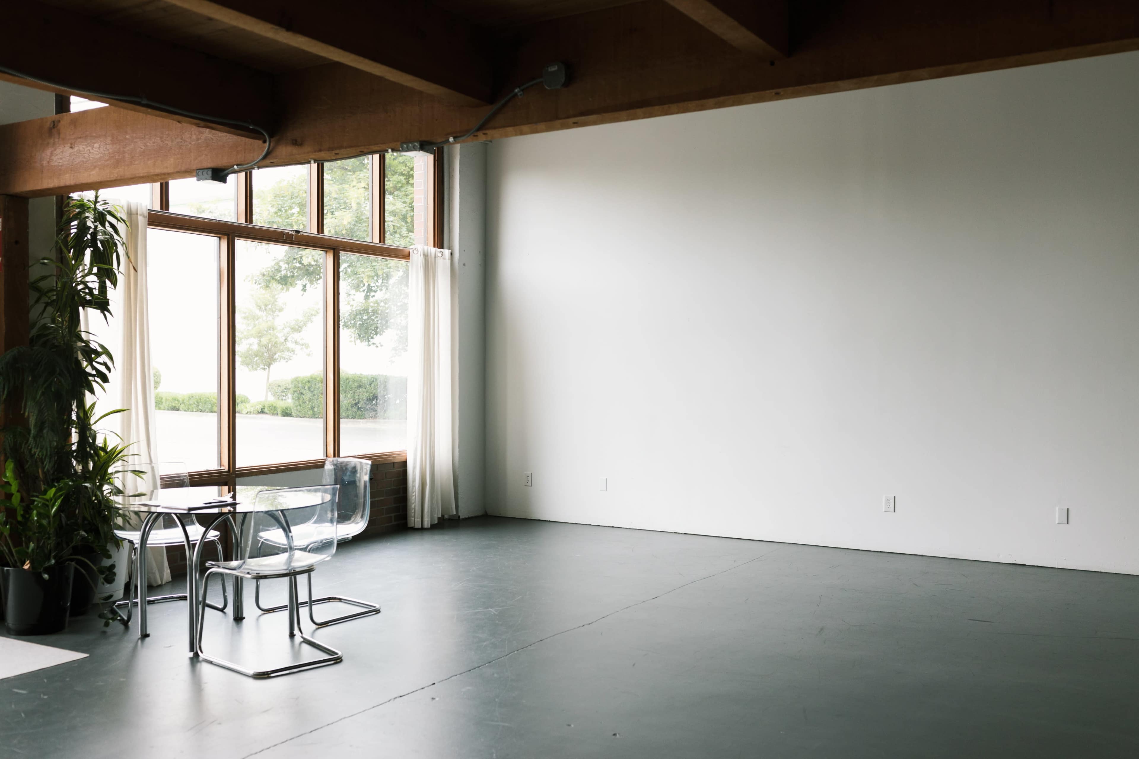 A spacious room features a glass table and chairs beside large windows with natural light streaming in.