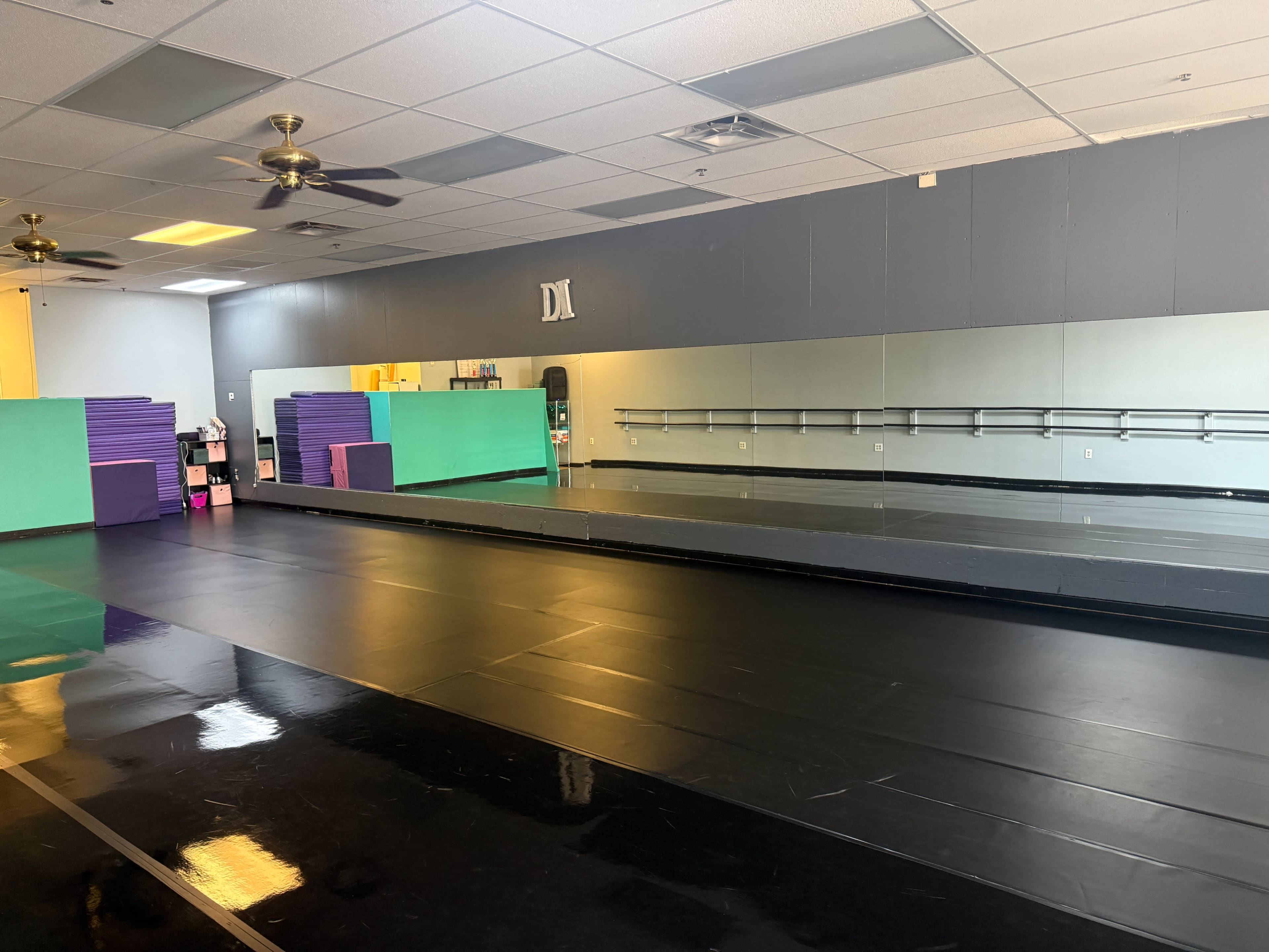 The image shows a dance studio with a mirrored wall, a black floor, and colorful foam blocks arranged against the wall.
