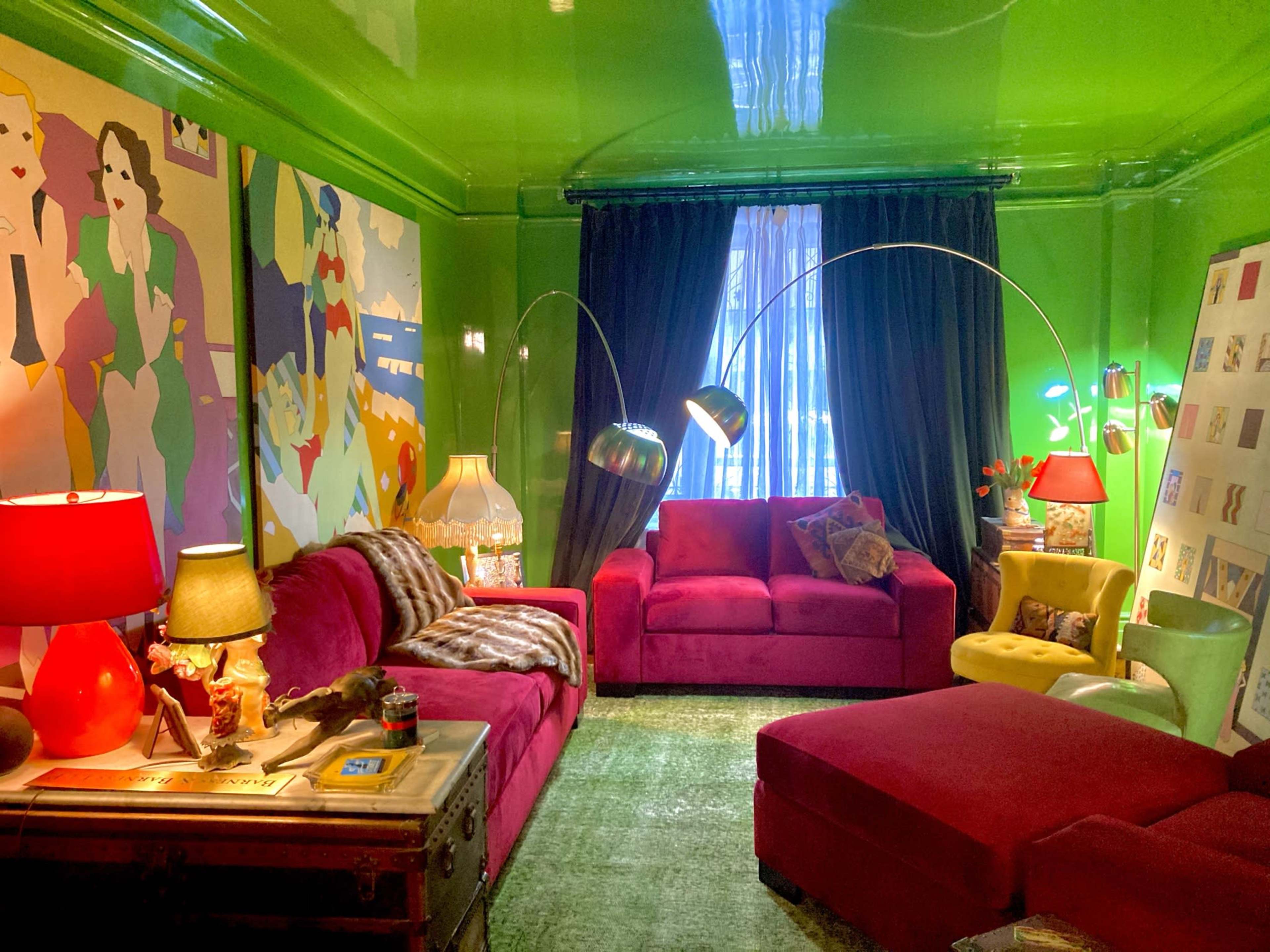 A vibrant living room with green walls, red sofas, colorful artwork, and various light fixtures.