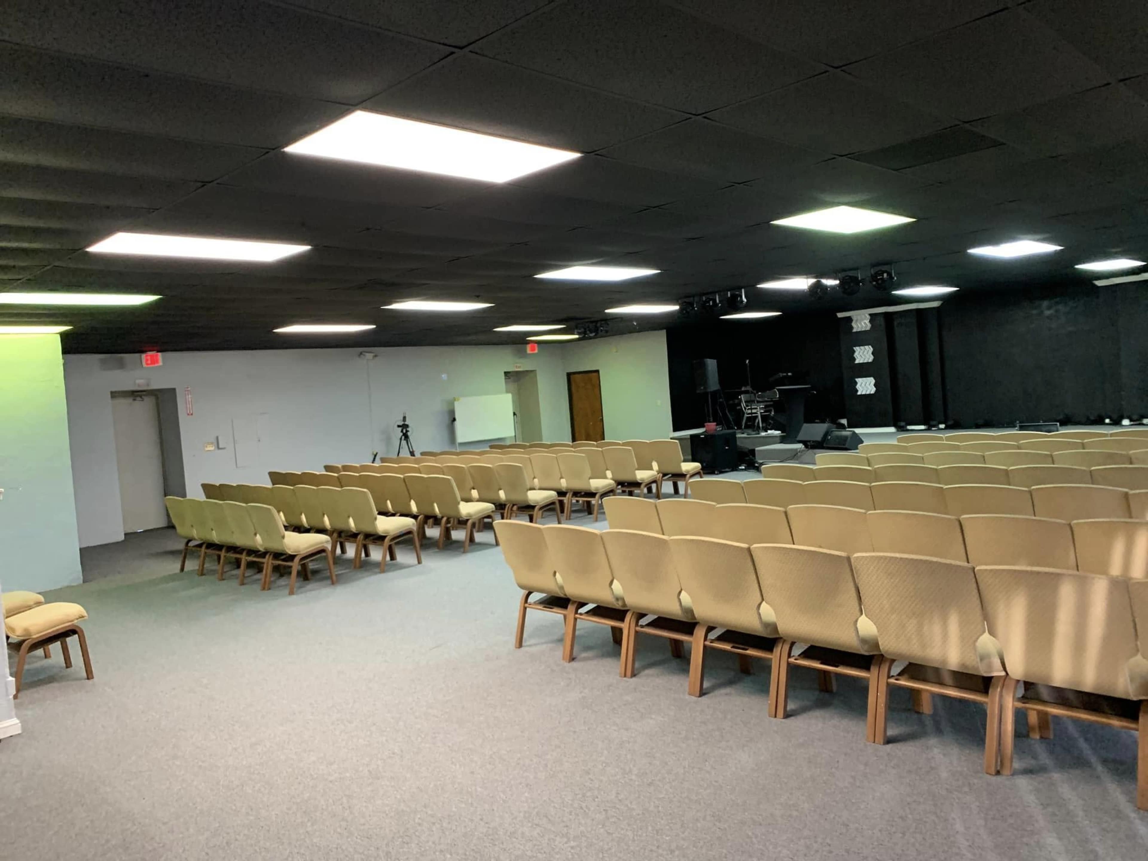 A spacious indoor area with rows of beige chairs facing a stage outfitted with musical instruments and sound equipment.