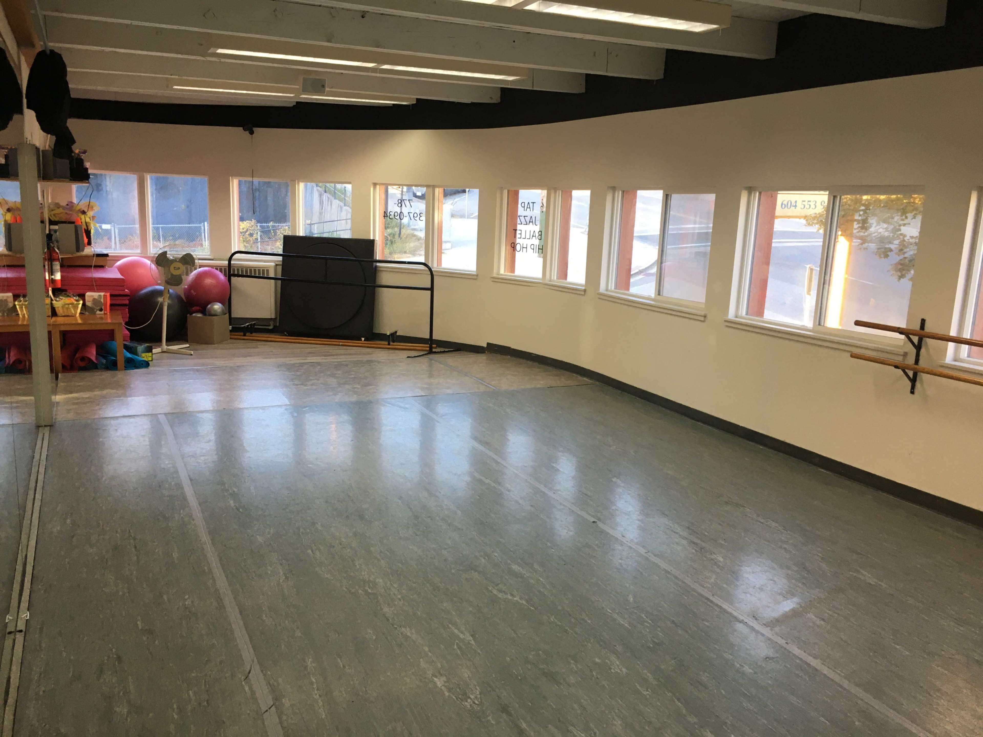 A spacious dance studio with large windows, wooden ballet bars, exercise equipment, and a smooth floor.