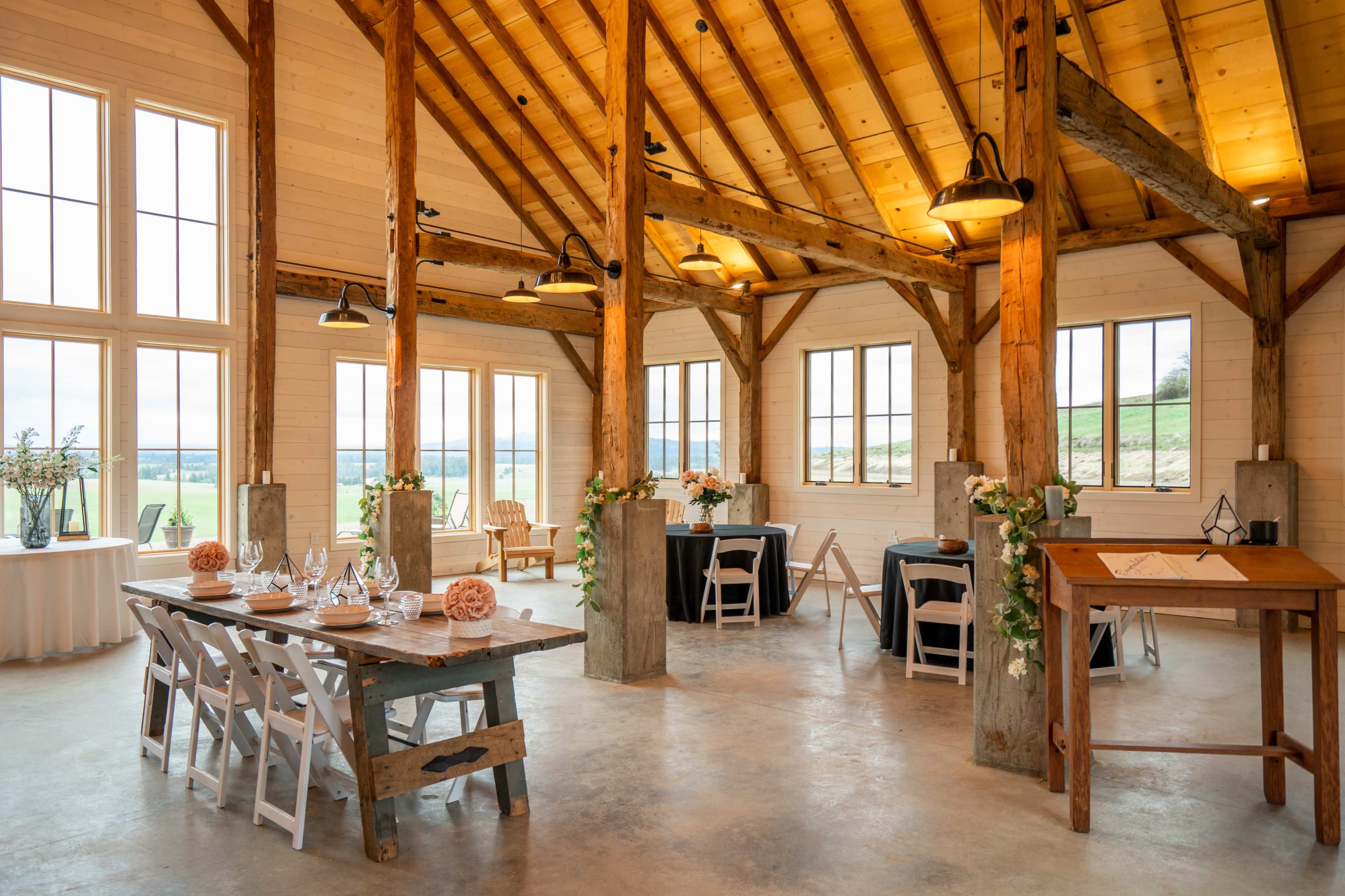 A spacious event venue with wooden beams, large windows offering a scenic view, and tables set for a gathering.