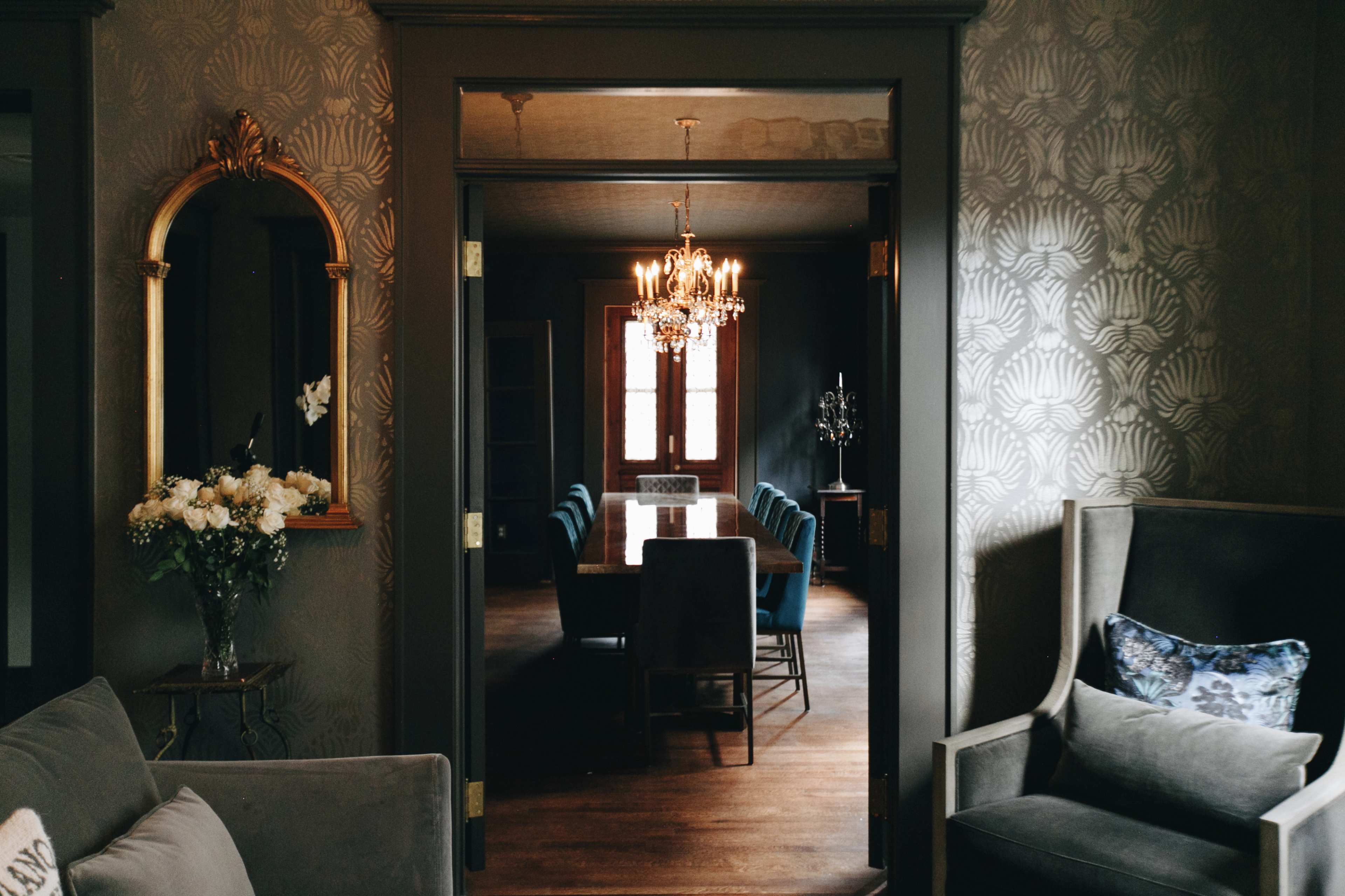 A dining room with a long table and chairs is visible through an open doorway, featuring a chandelier overhead and floral decorations.