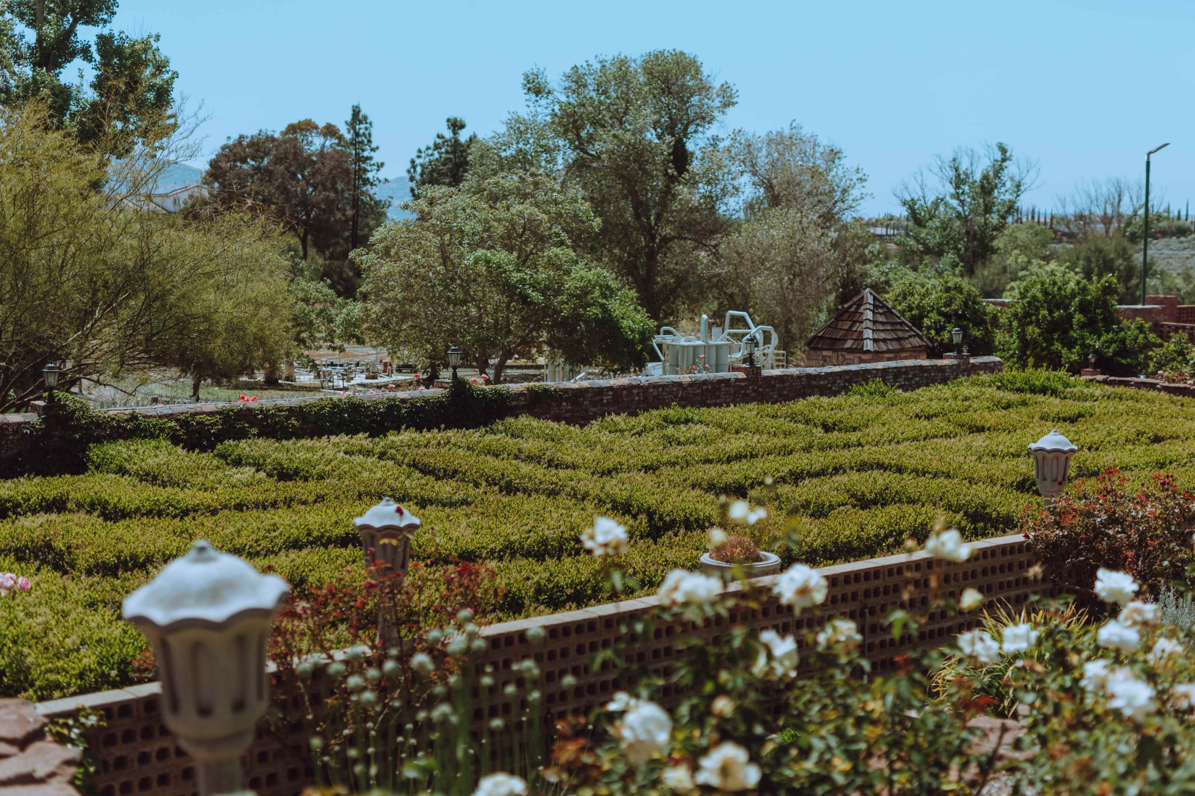 The image shows a landscaped garden with neatly arranged hedges, trees in the background, and flower beds in the foreground.