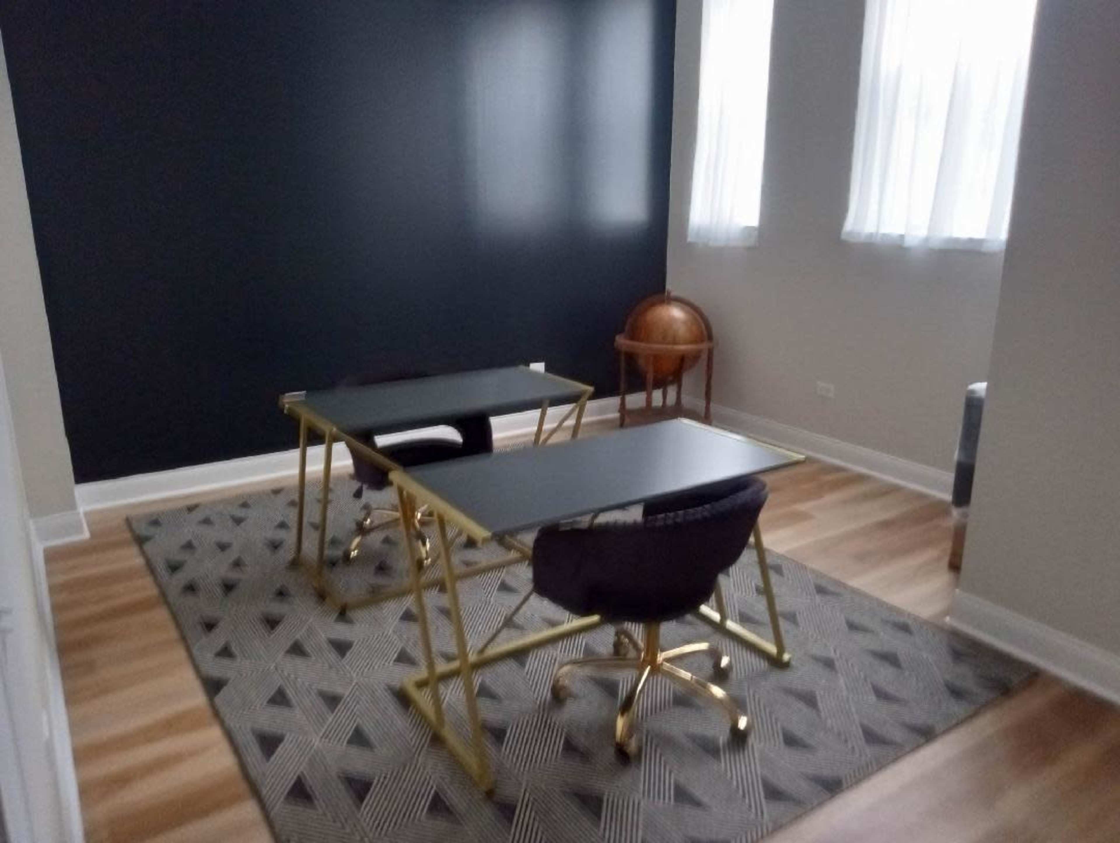 The image shows a modern office space with two desks, each accompanied by a chair, set against a dark wall and featuring a globe in the corner.