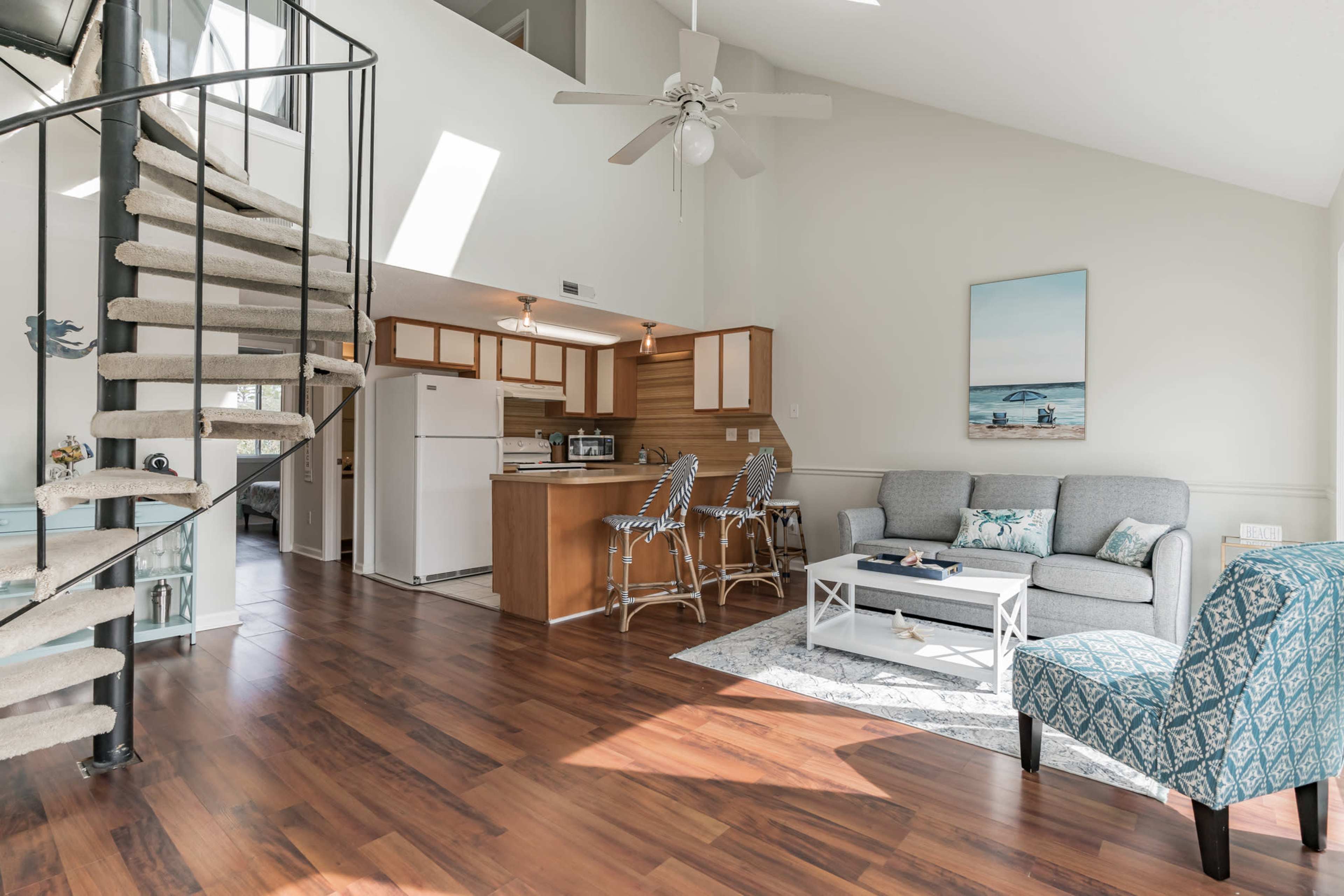 A modern open-concept living area with a spiral staircase, kitchen, and seating arrangement featuring a gray sofa and a patterned armchair.