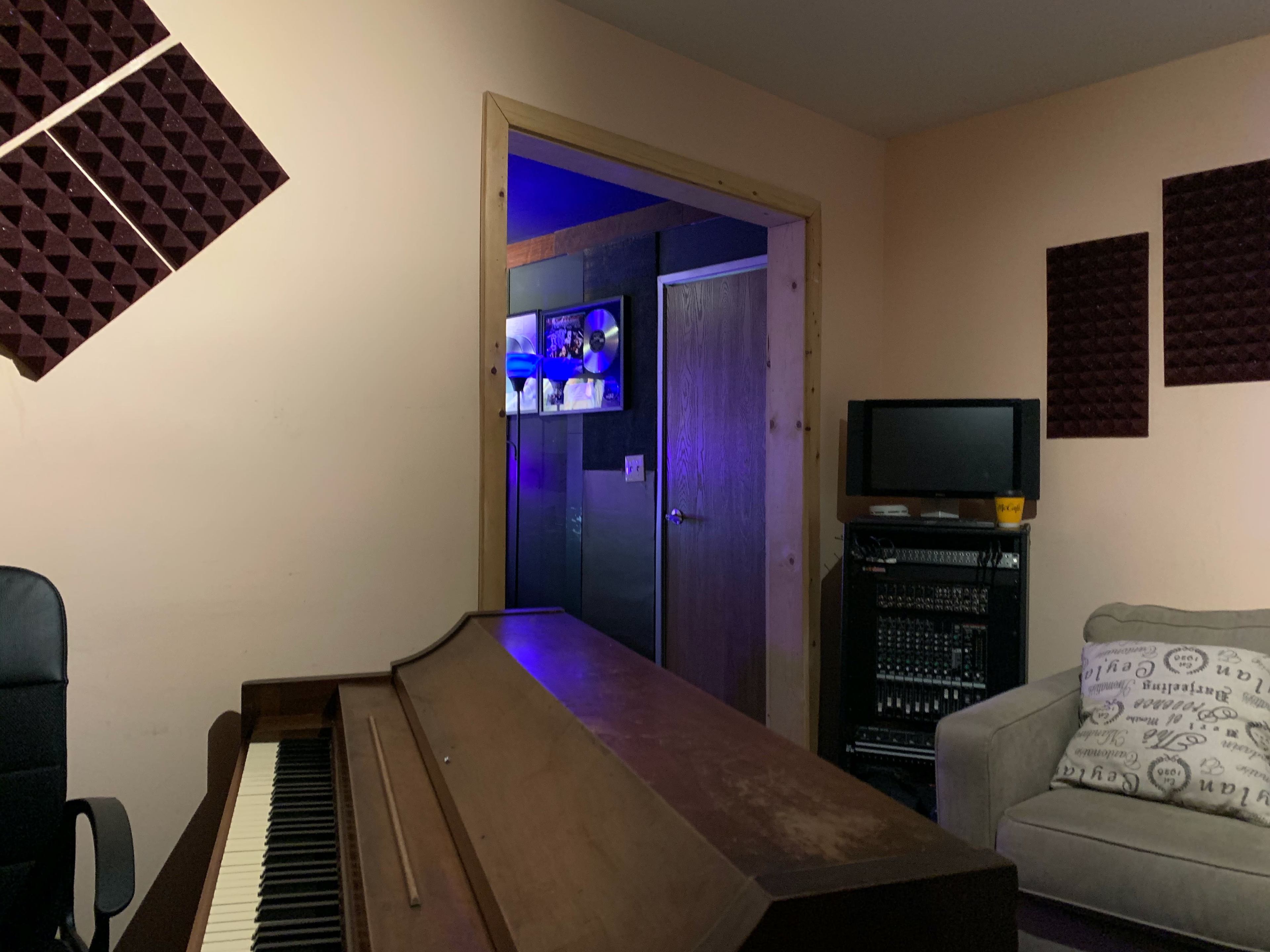 A room with a piano, a chair, and soundproofing panels on the walls, along with a television and audio equipment in the corner.