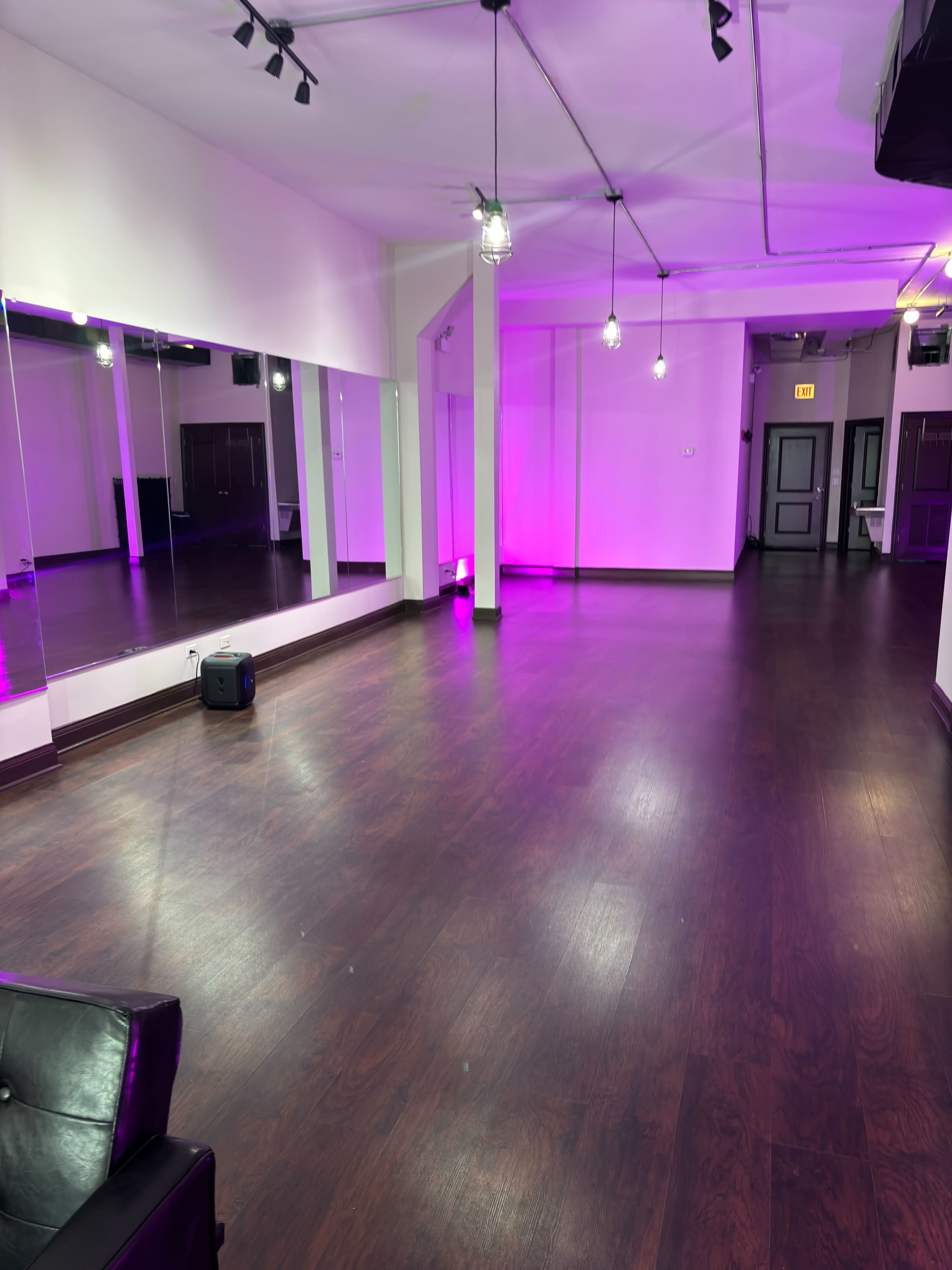 A spacious, well-lit dance studio with mirrors on one wall and purple lighting accents.