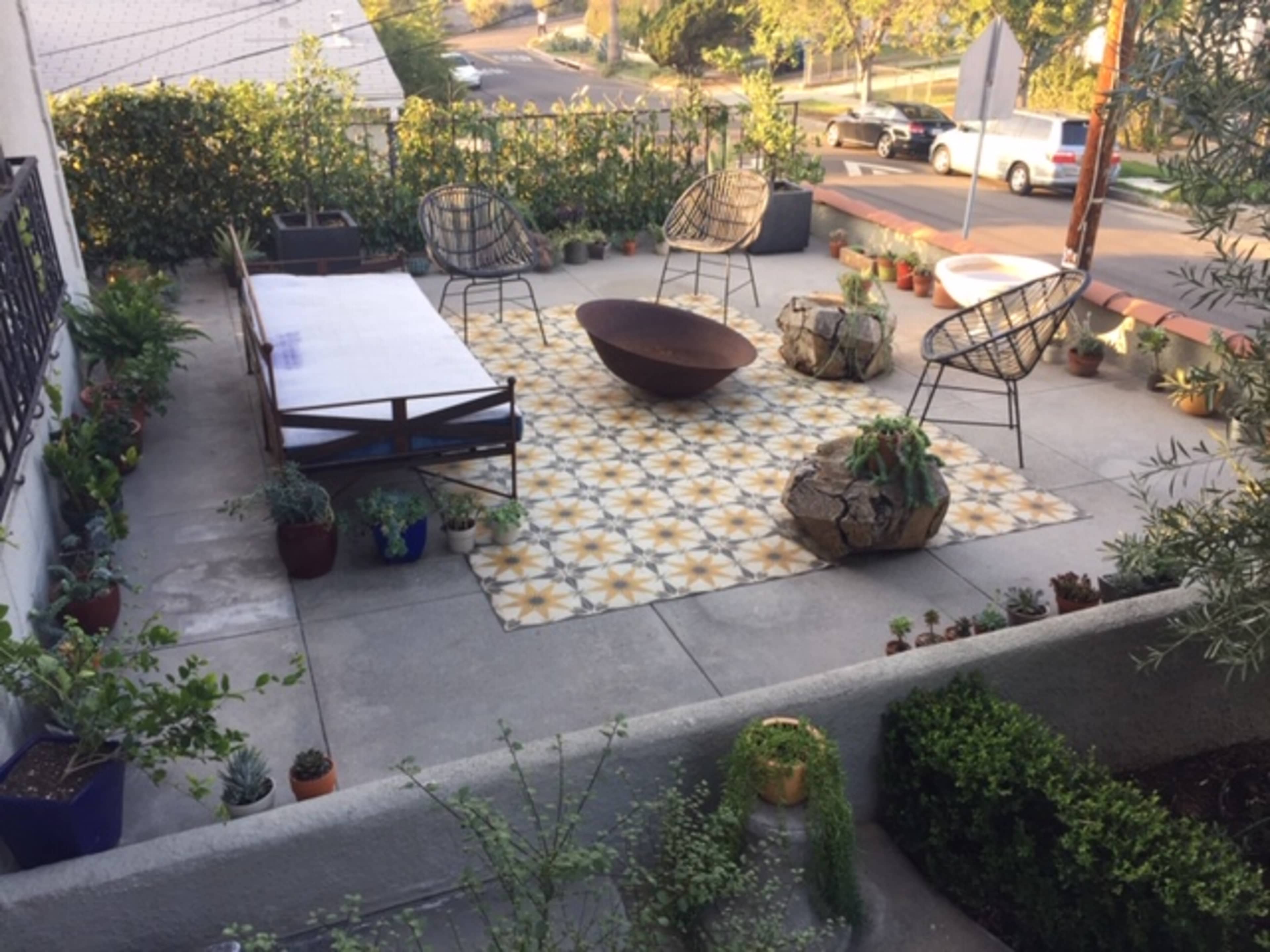 A tiled patio features a low table, four chairs, and various potted plants.