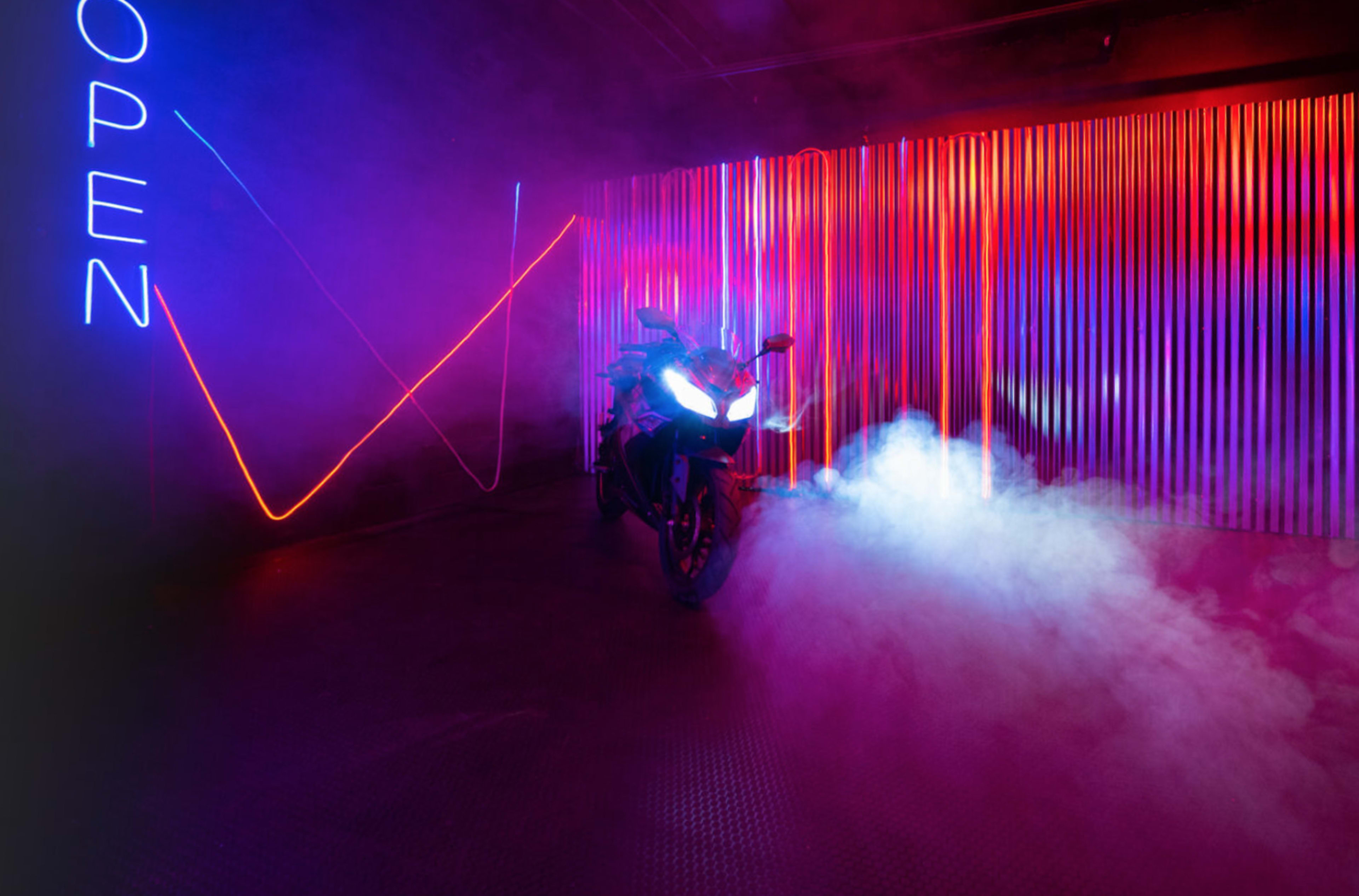 A motorcycle is parked in a dimly lit space with colorful neon lights and smoke effects.