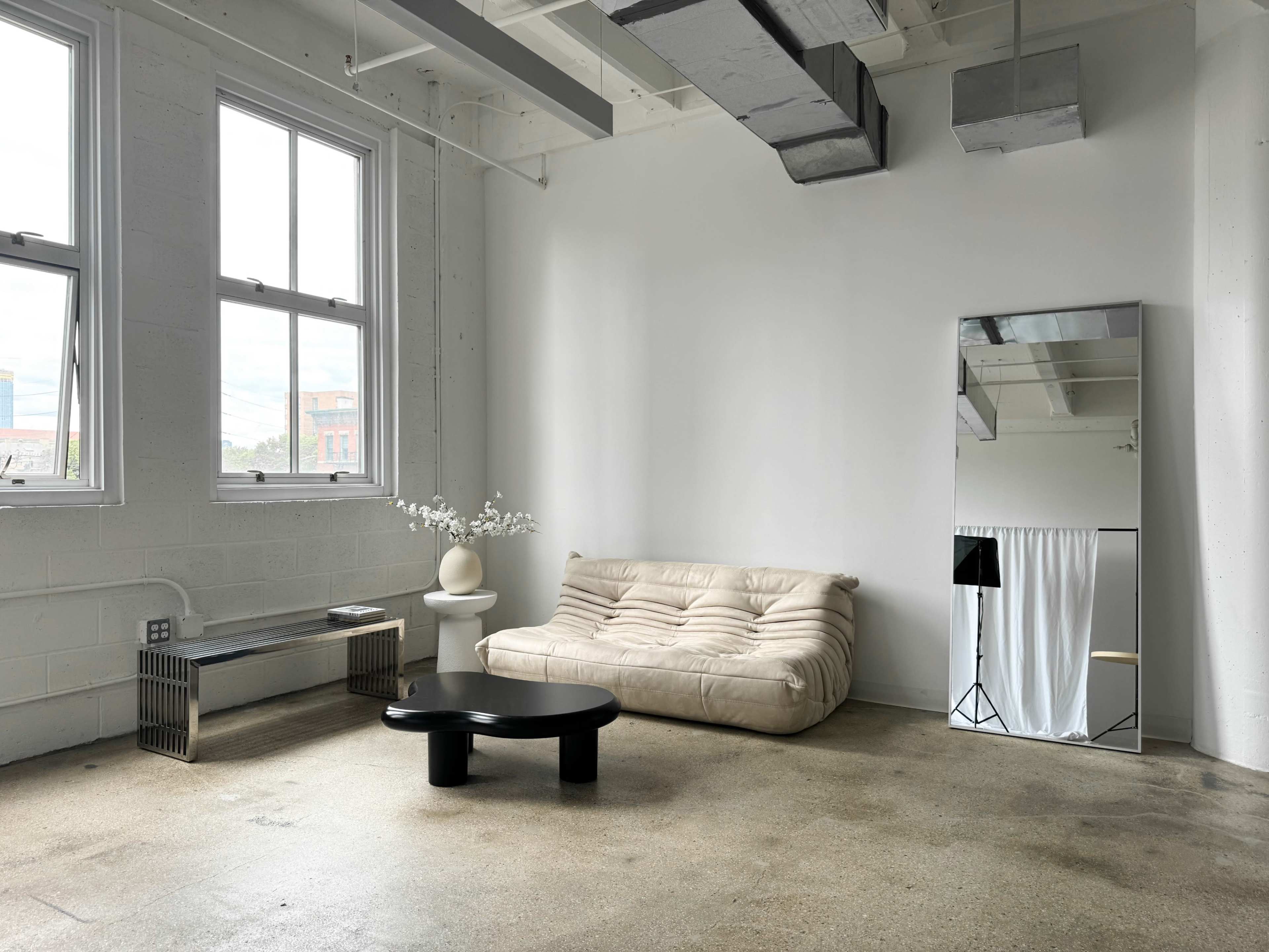 A minimalist room featuring a white couch, a black coffee table, a large mirror, and a plant on a side table.