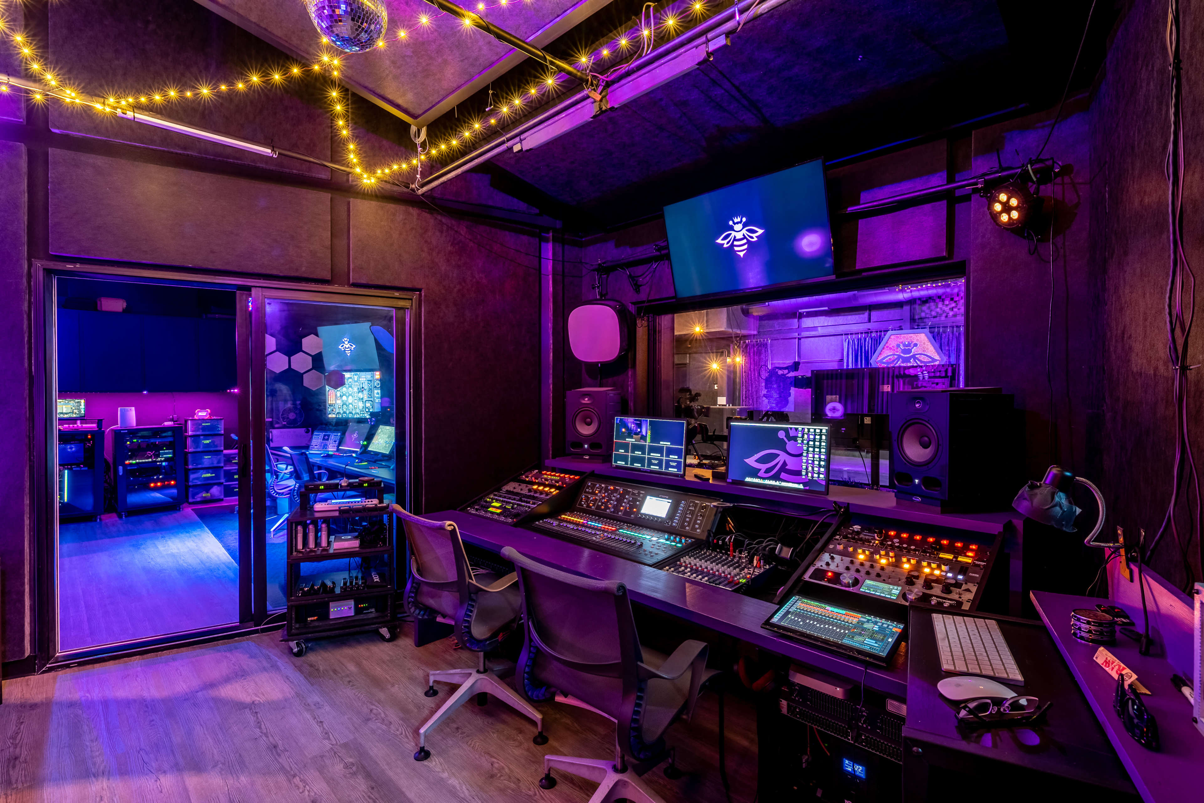 The image shows a modern recording studio with a control desk equipped with various audio controls and monitors, surrounded by purple and warm lighting.