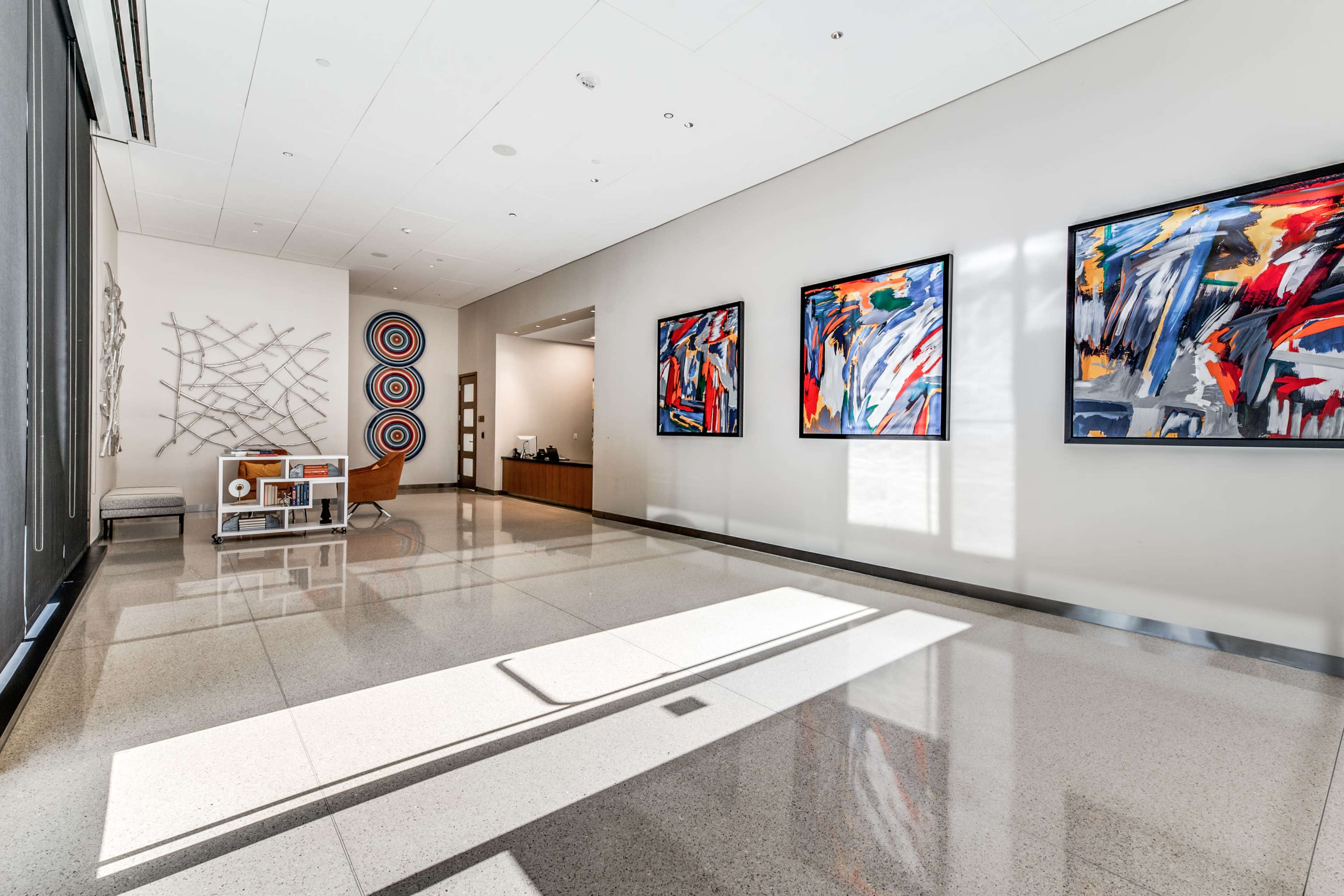 The image shows a modern lobby featuring colorful abstract artwork on the walls and polished stone flooring.